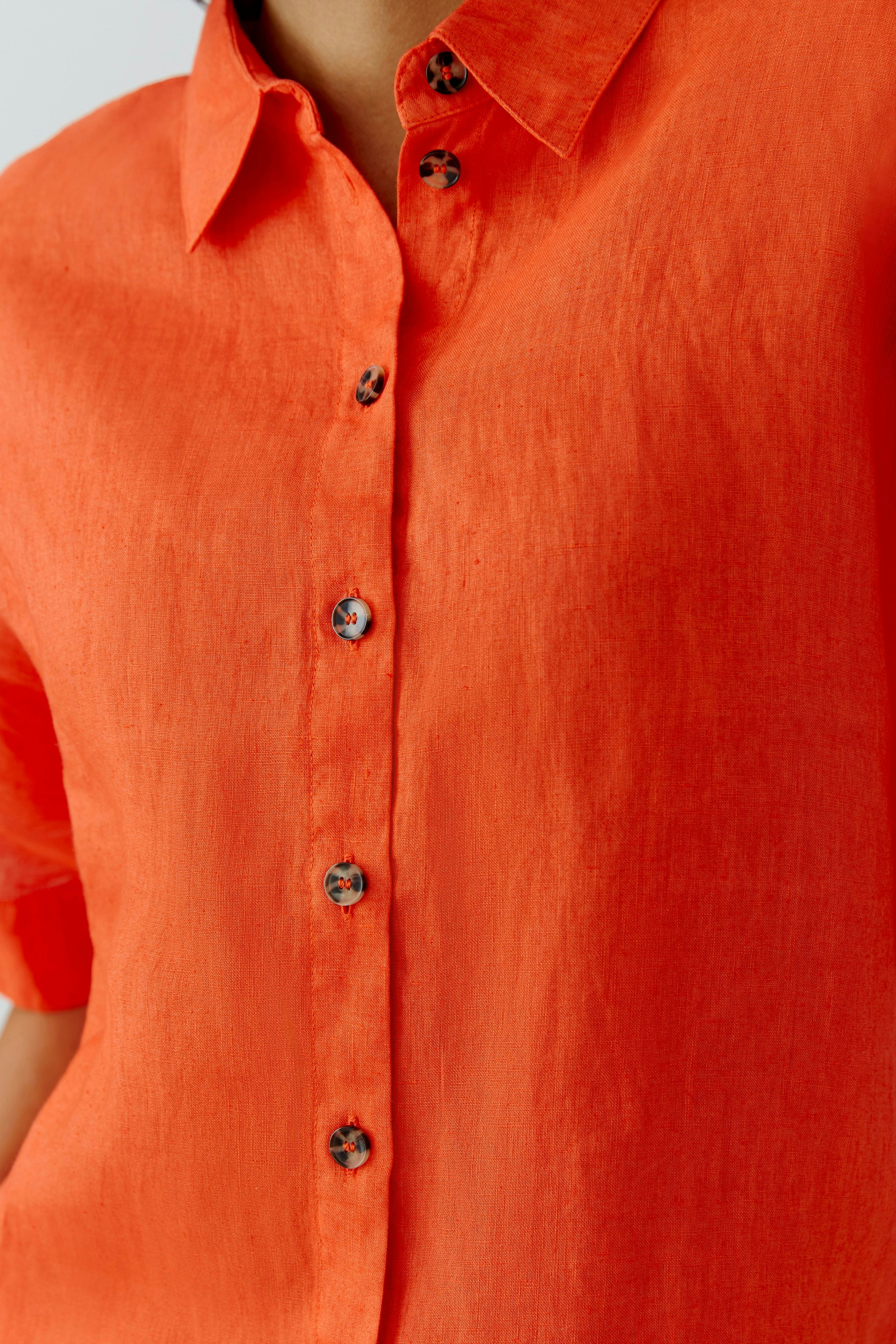 Casual women's blouse: Close-up of a woman in a vibrant orange button-up blouse with short sleeves.