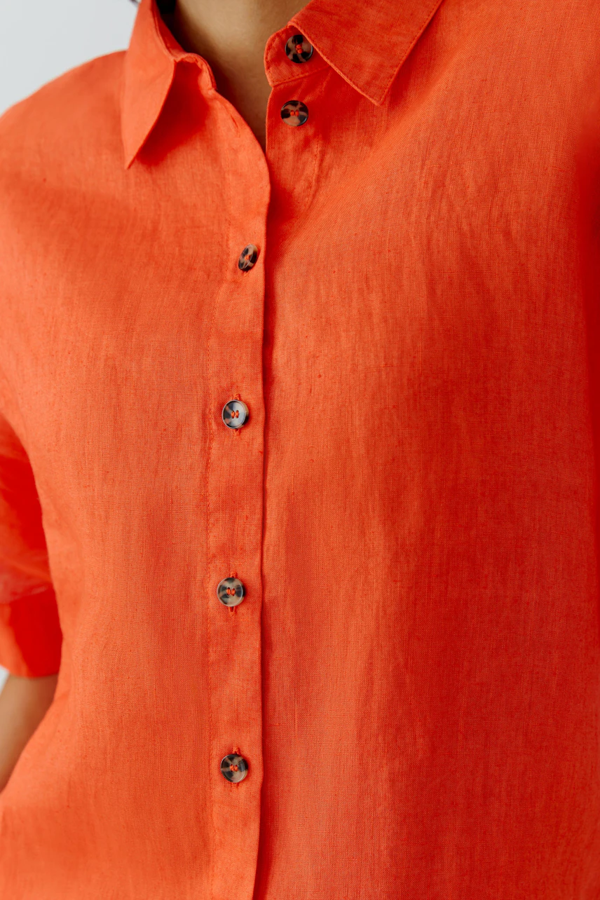 Casual women's blouse: Close-up of a woman in a vibrant orange button-up blouse with short sleeves.