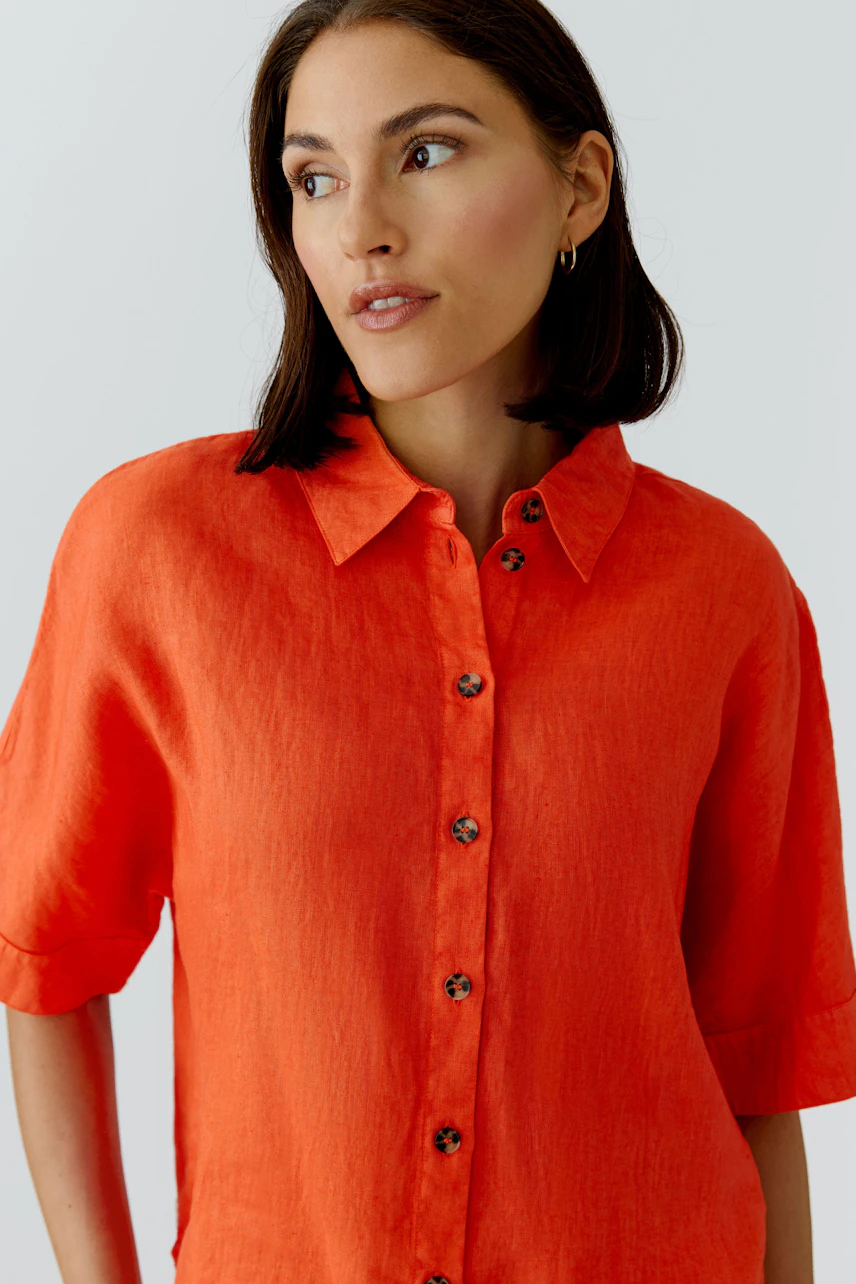 Casual women's blouse: A woman in a bright orange button-up blouse with short sleeves.