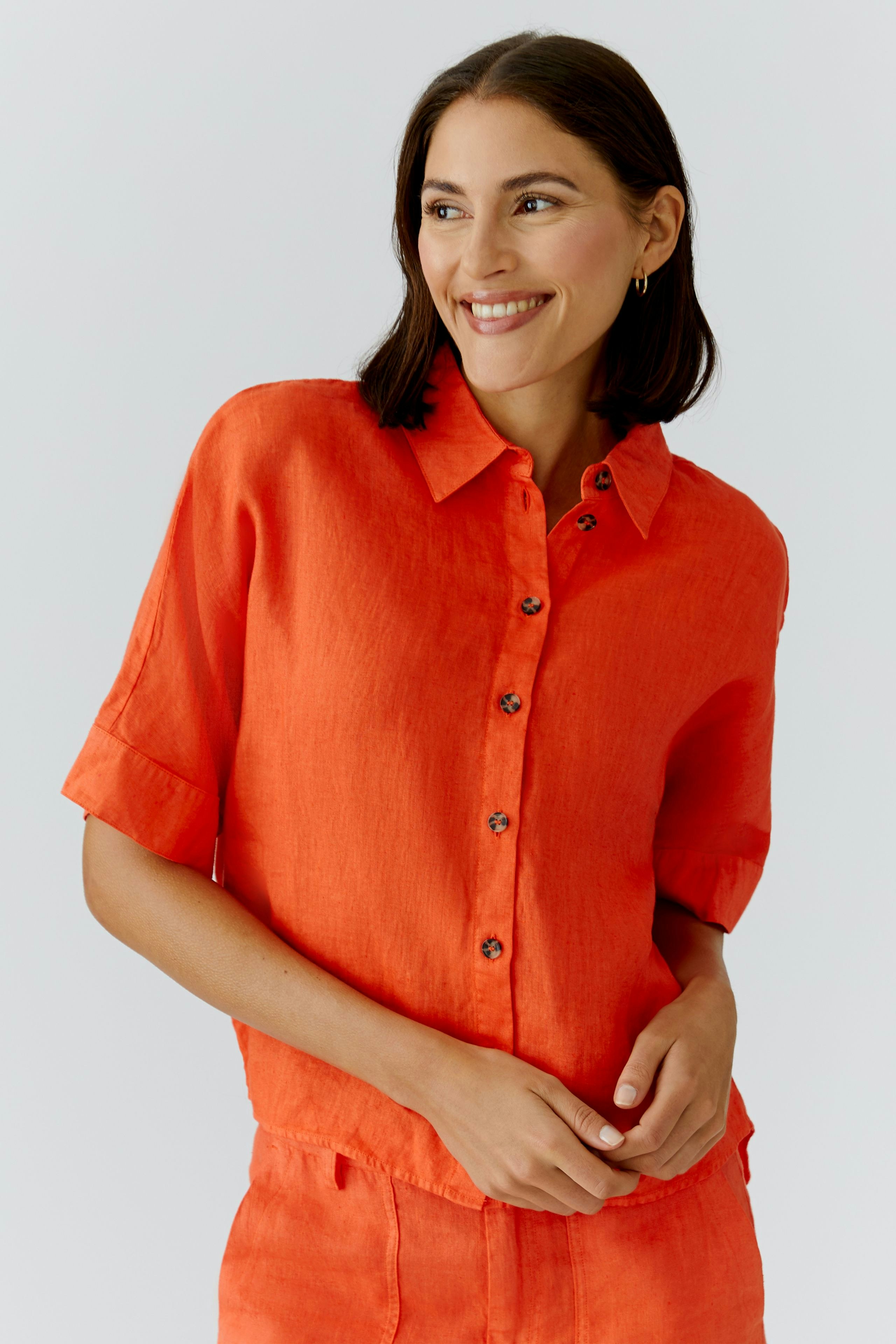 Casual women's blouse: Smiling woman in a bright orange button-up blouse with short sleeves.
