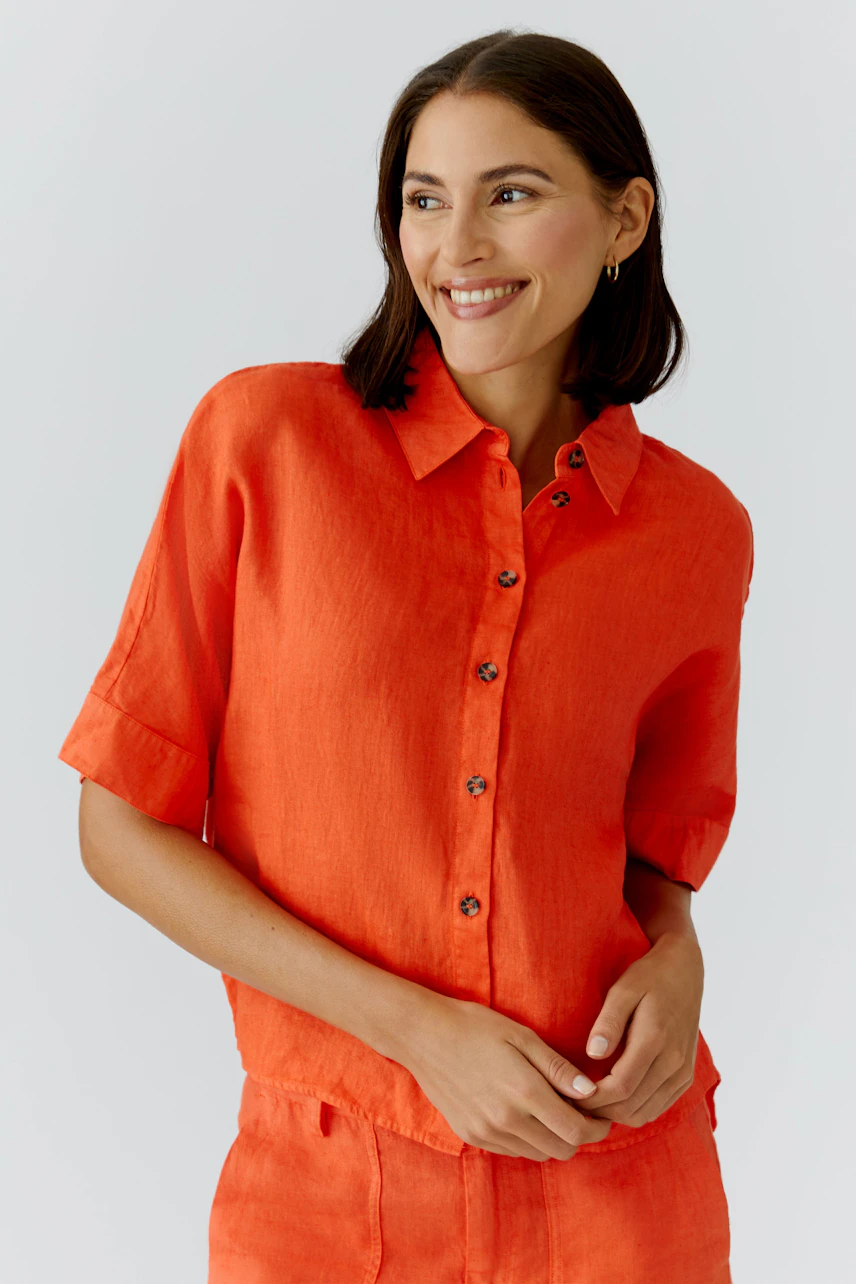 Casual women's blouse: Smiling woman in a bright orange button-up blouse with short sleeves.