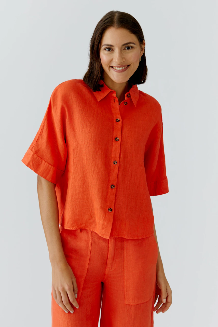 Casual women's blouse: A woman in a bright orange button-up blouse with short sleeves smiles confidently.
