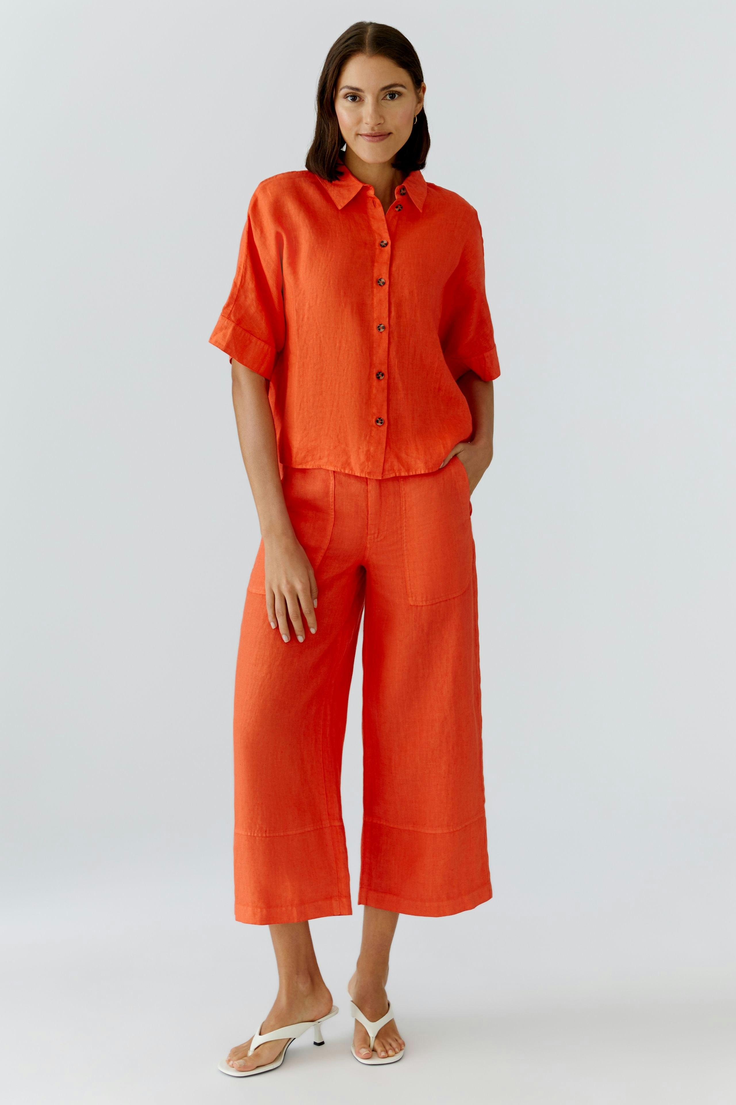 Casual women's blouse: A woman in a bright orange button-up blouse paired with wide-leg pants.