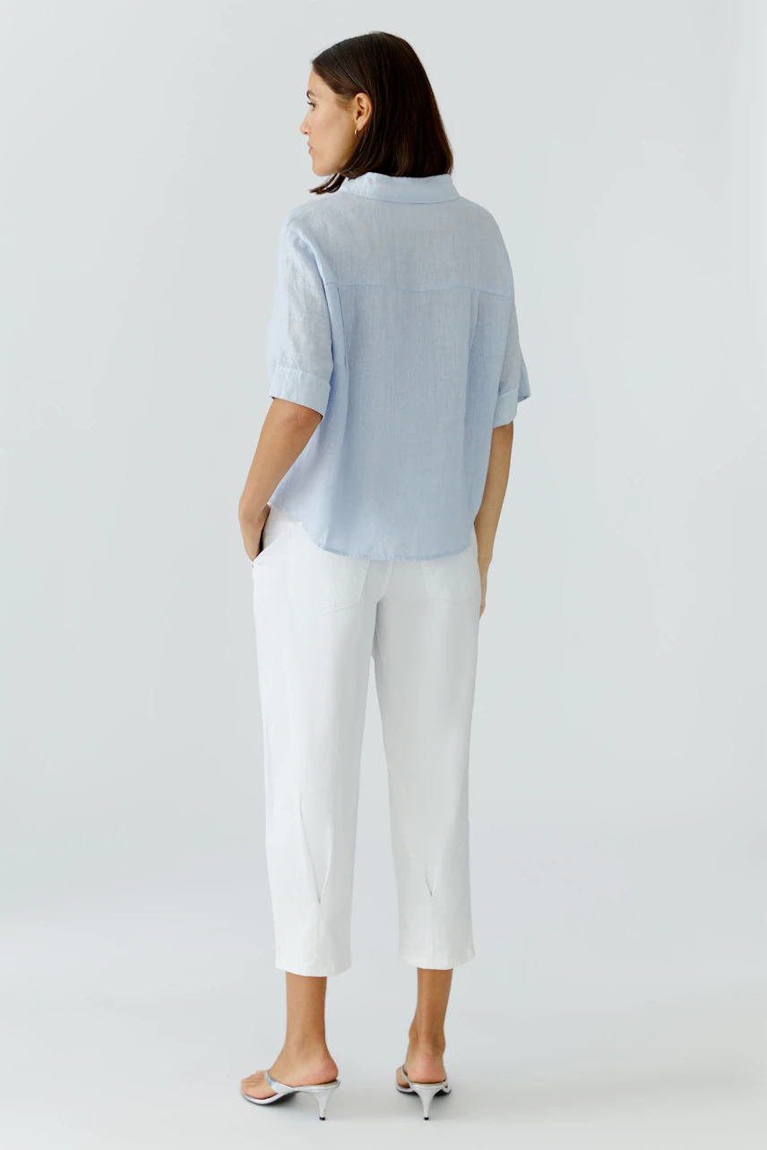 Light blue blouse: Woman wearing a relaxed-fit short-sleeve blouse with a back yoke.