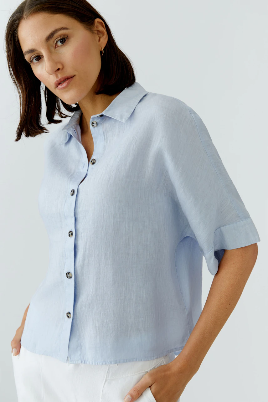 Light blue blouse: Woman in a short-sleeve button-up shirt, styled casually with a relaxed fit.