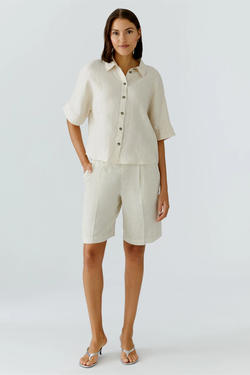 Casual women's blouse: A woman in a light linen blouse with buttons and relaxed fit shorts.