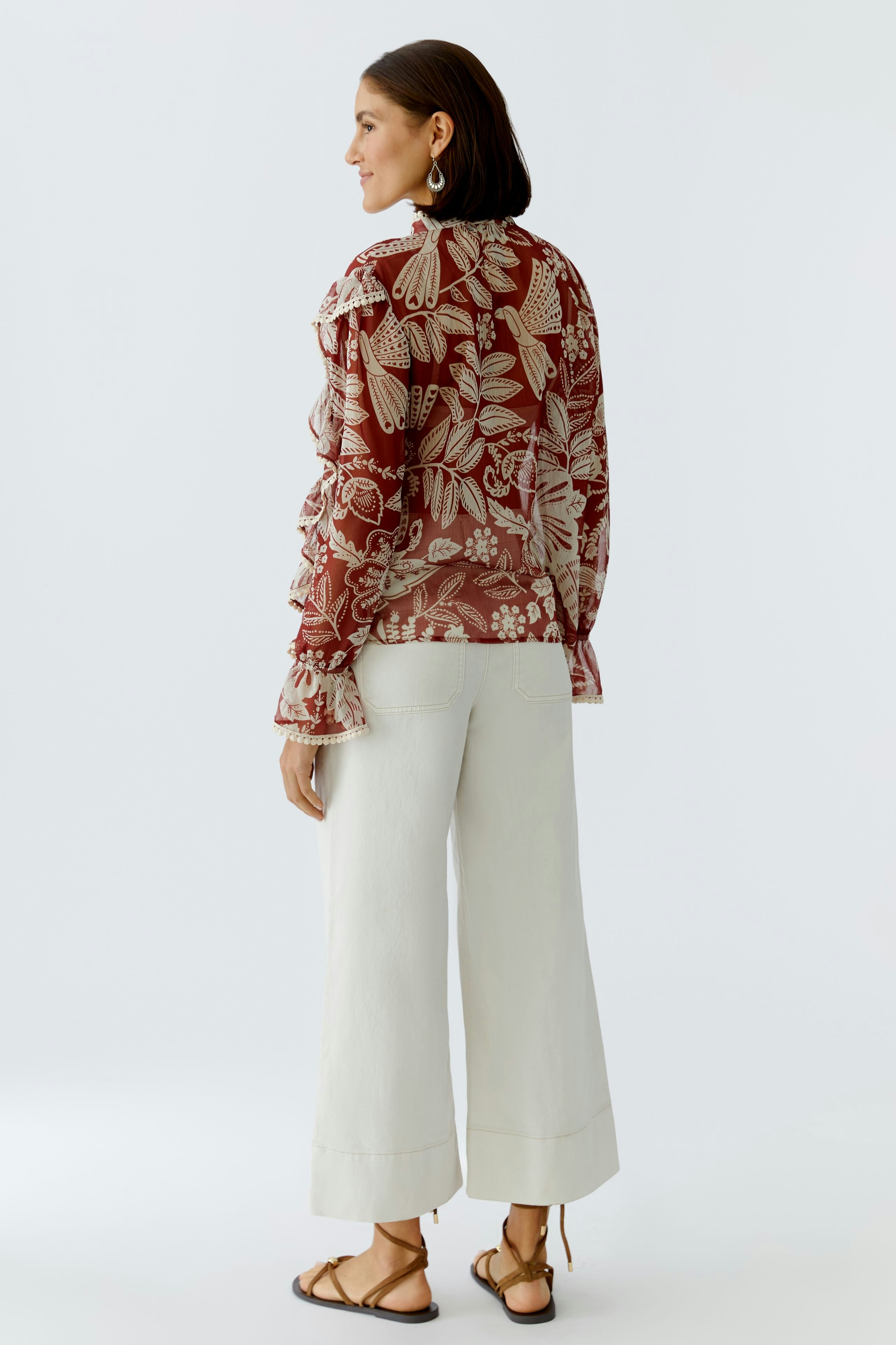 Damen-Bluse: Frau in floraler Bluse mit Rüschen und hellen, weiten Hosen.