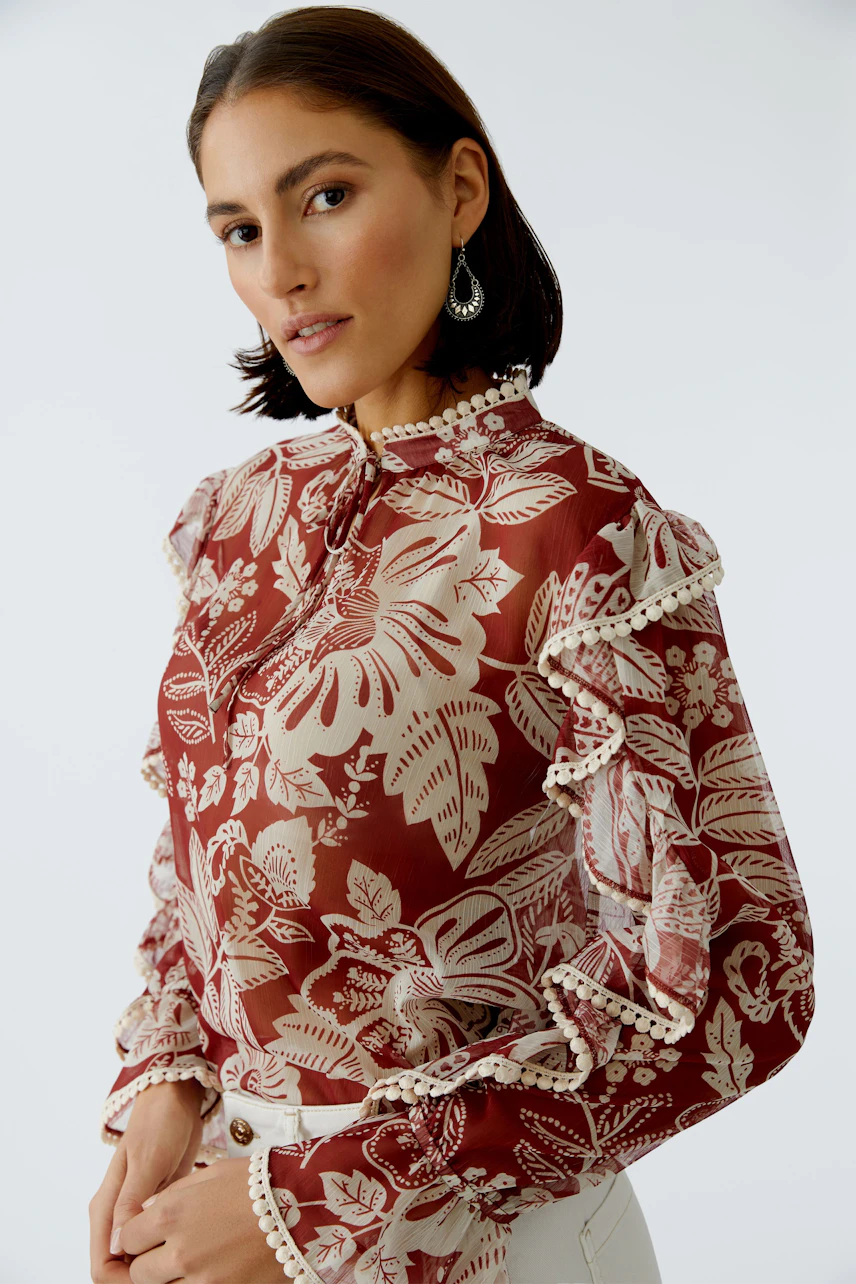 Damen-Bluse: Frau in roter Bluse mit floralem Muster und Rüschen, lässig und modern.