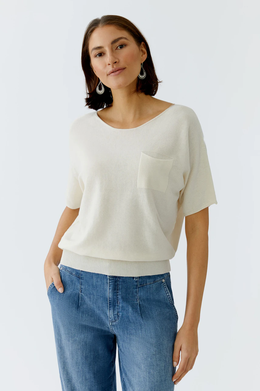 Casual women's pullover: A woman in a light cream pullover with a pocket, paired with blue jeans.