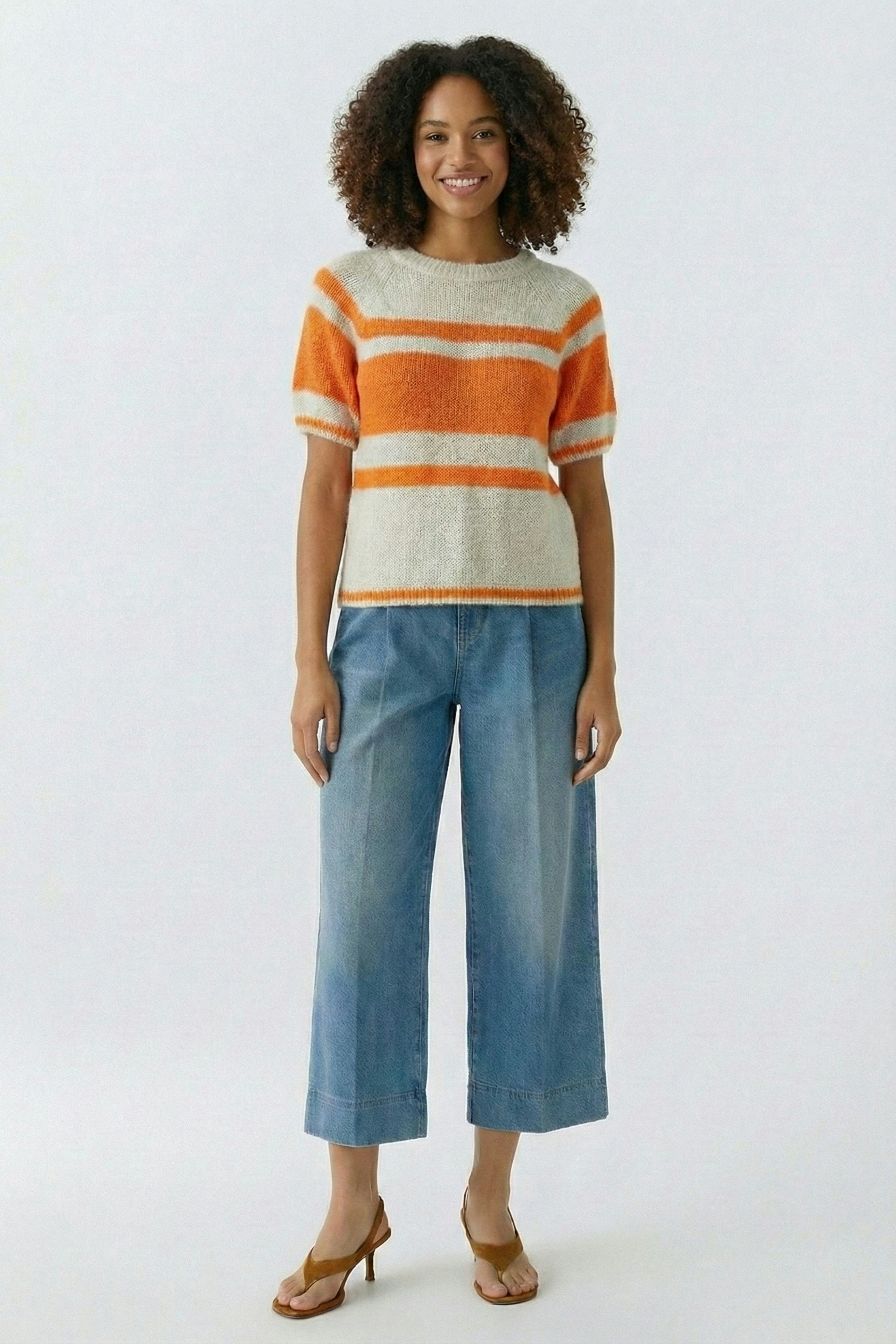 Damen-Pullover: Frau in gestreiftem, orange-weißen Pullover mit lässigen Jeans und Sandalen.