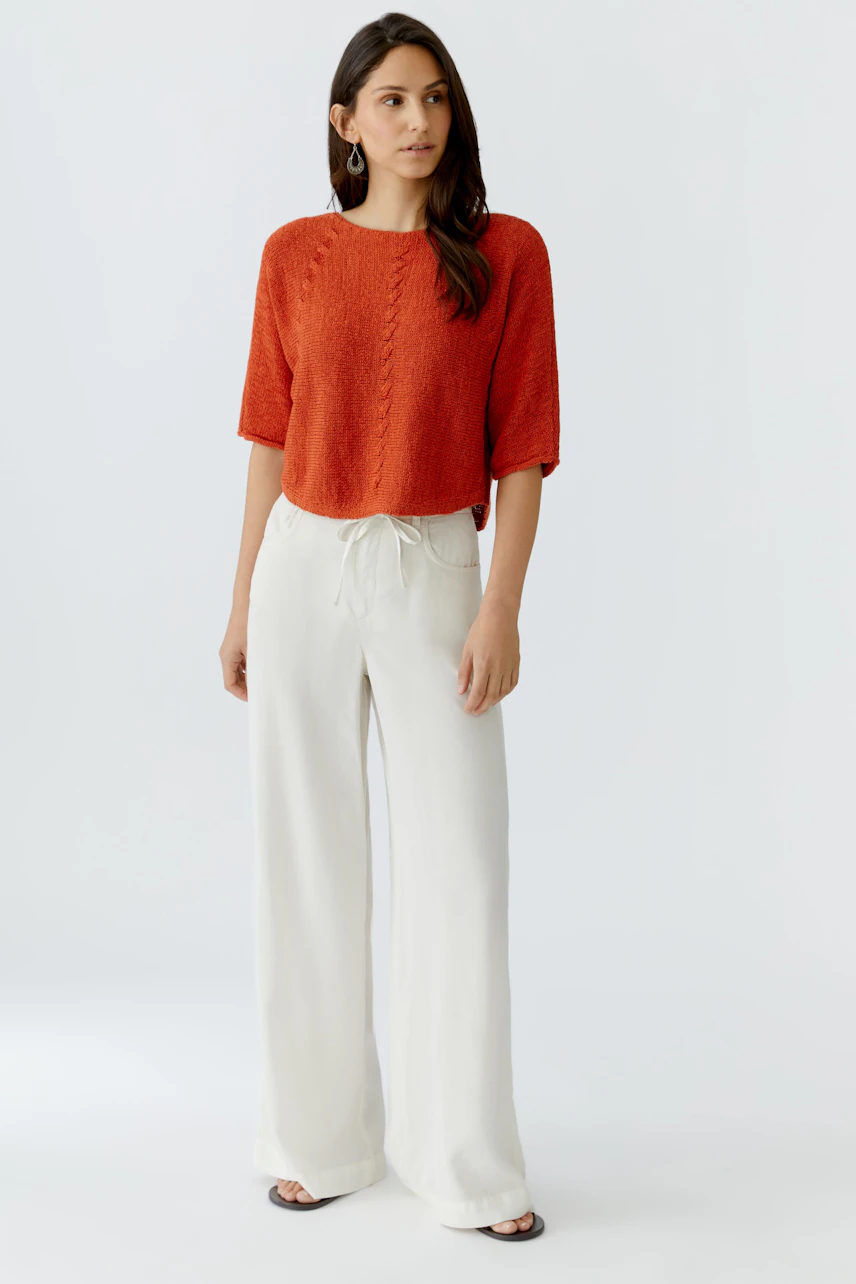 Casual women's pullover: Young woman in a short-sleeved, textured red pullover paired with light trousers.