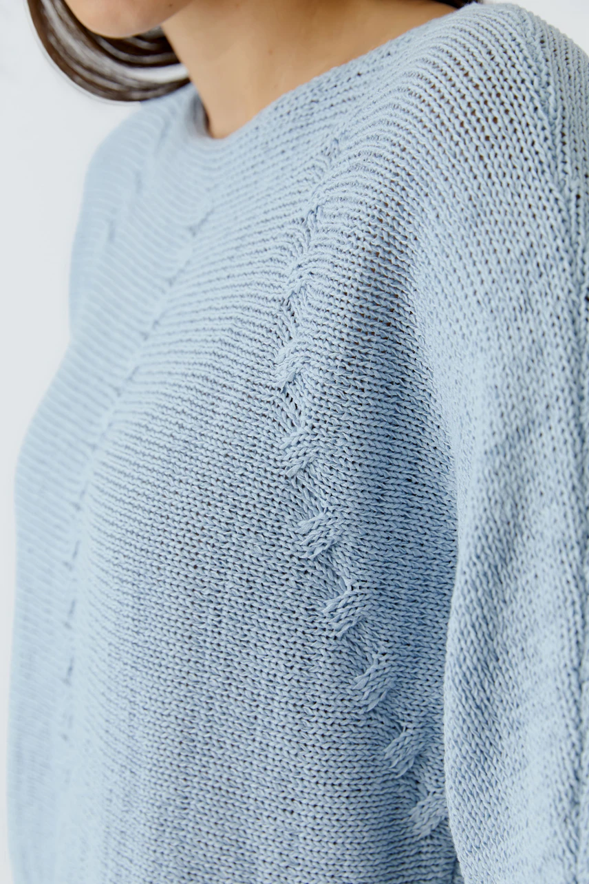 Casual women's pullover: Close-up of a woman in a light blue knitted pullover with textured details.