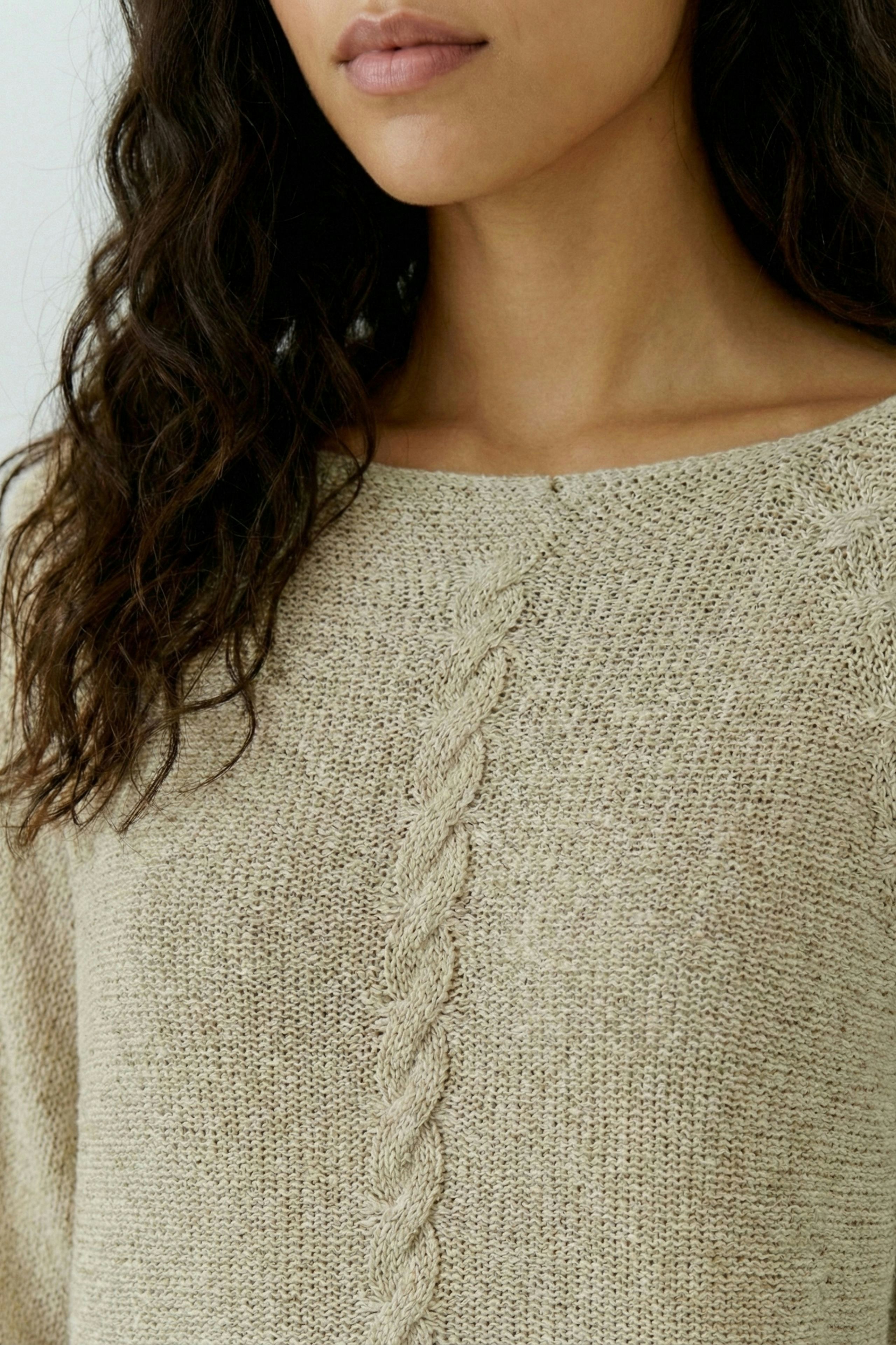 Beiger Damen-Pullover: Frau mit lockigem Haar trägt einen lässigen Strickpullover mit Zopfmuster.