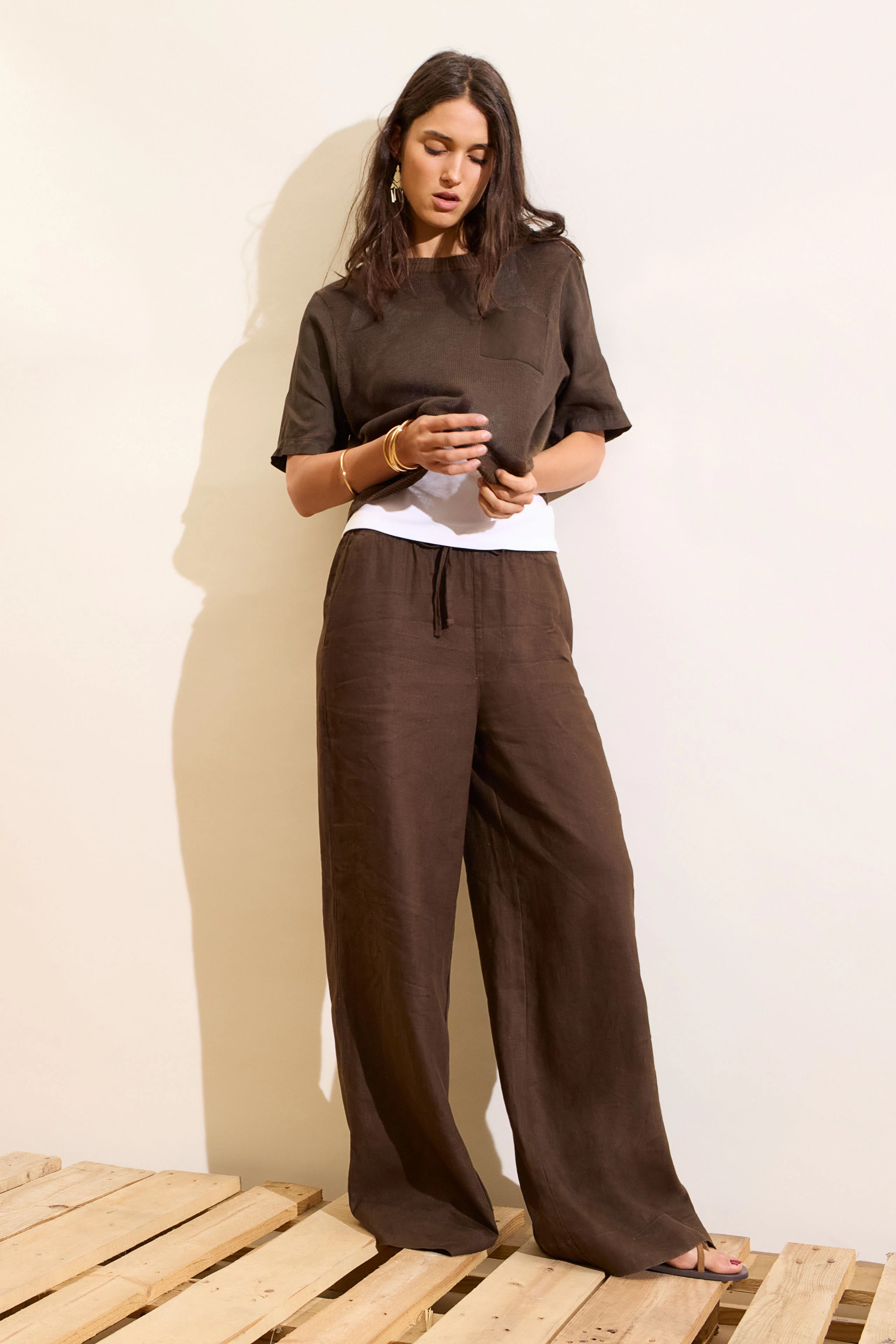 Lässiger Damen-Pullover: Frau im braunen Pullover und Hose, entspannt auf Holzpalette stehend.