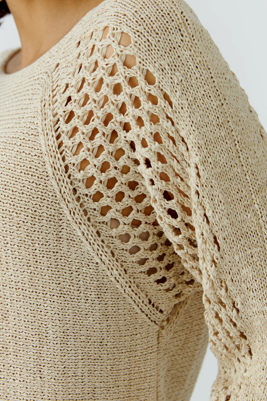 Casual women's pullover: Close-up of a woman in a light beige knitted pullover with openwork sleeves.