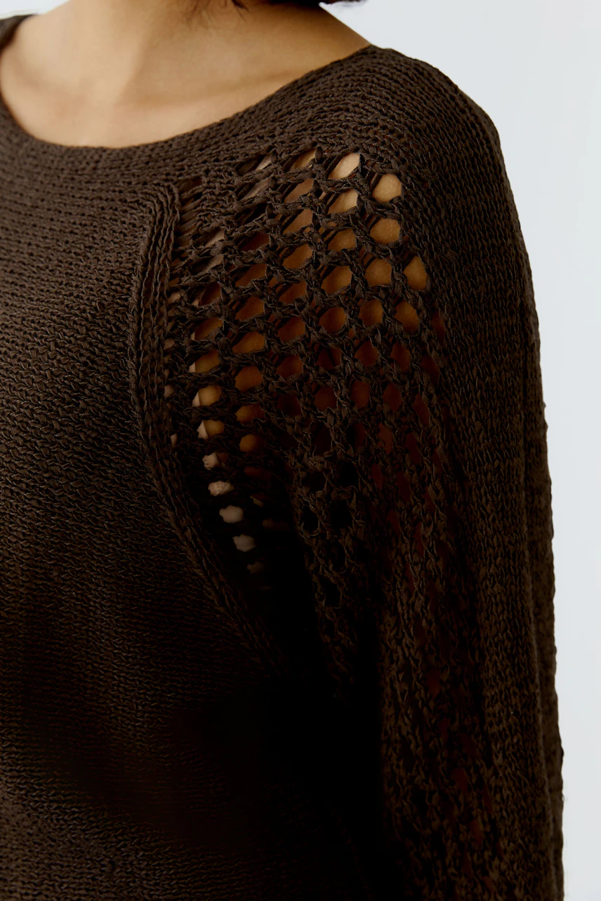 Modern women's pullover: A woman in a brown knitted pullover with openwork sleeves.