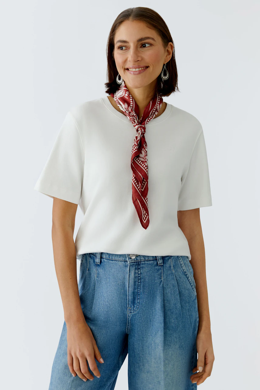 Stylish women's scarf: A woman wearing a red patterned scarf with a white top and relaxed jeans.