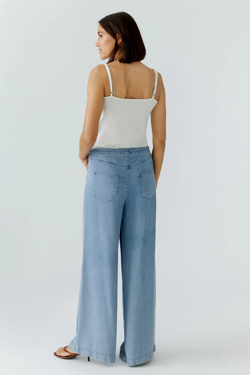 Lässige Damen-Hose: Frau in hellblauer, weit geschnittener Jeanshose und weißem Top von hinten.