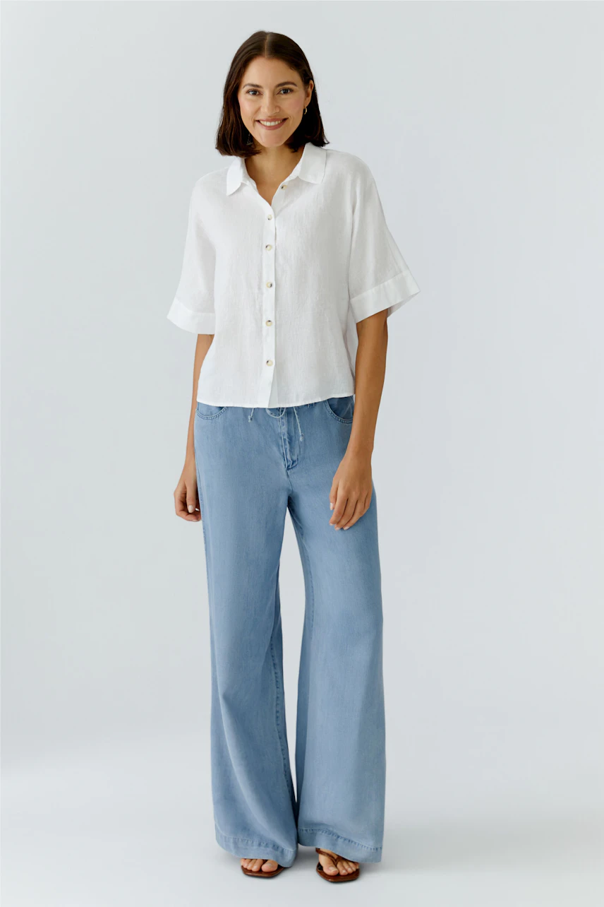Lässige Damen-Hose: Frau in hellblauer, weiter Jeanshose und weißer Bluse lächelt entspannt.