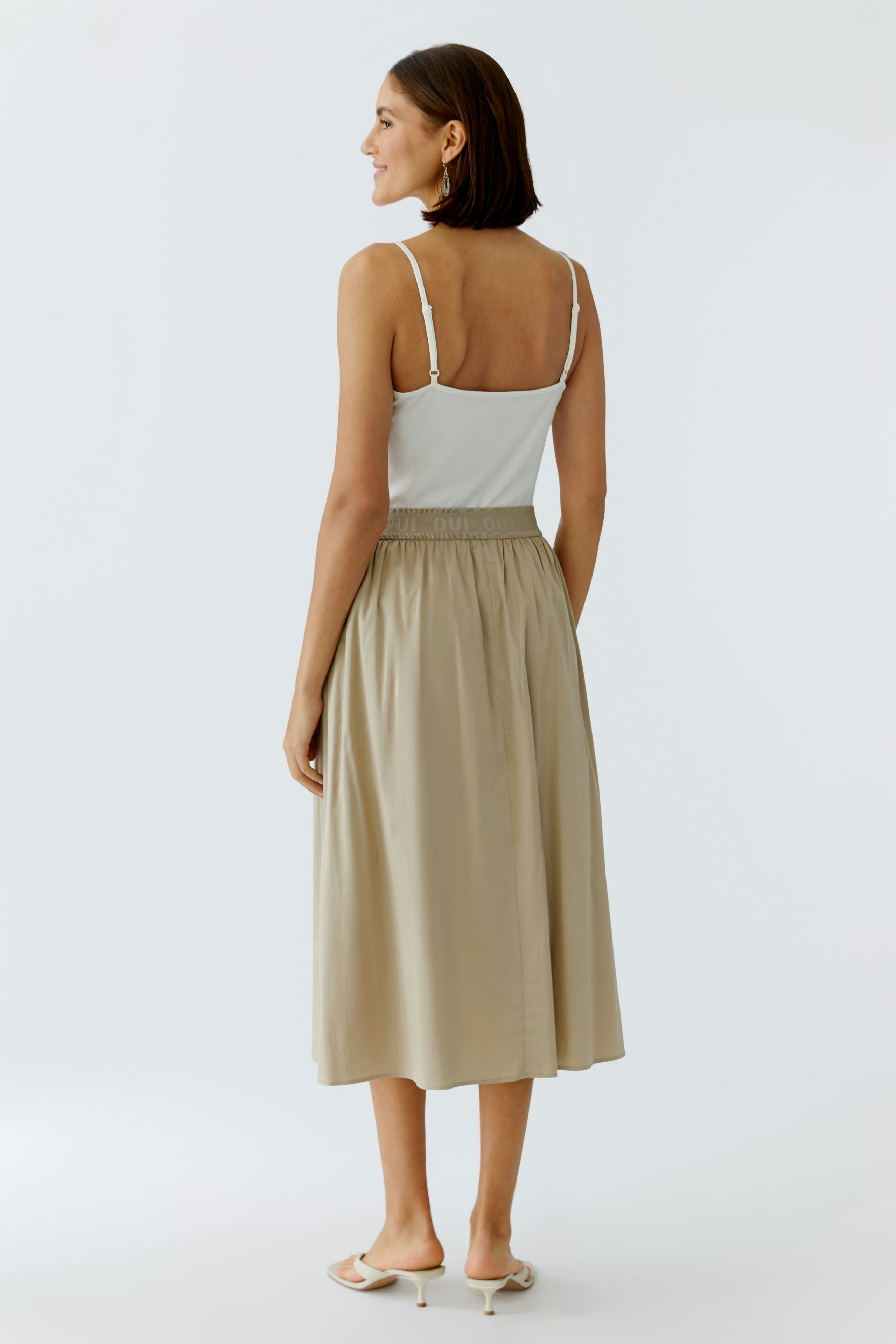 Beiger Midirock: Frau mit Spaghettiträger-Top zeigt den fließenden Rock mit elastischem Bund.