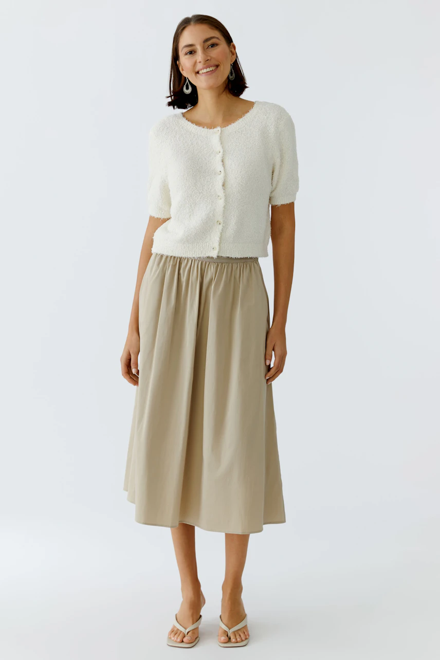 Casual midirock: Woman in a light beige midiskirt with an elastic waistband, paired with a soft cardigan.