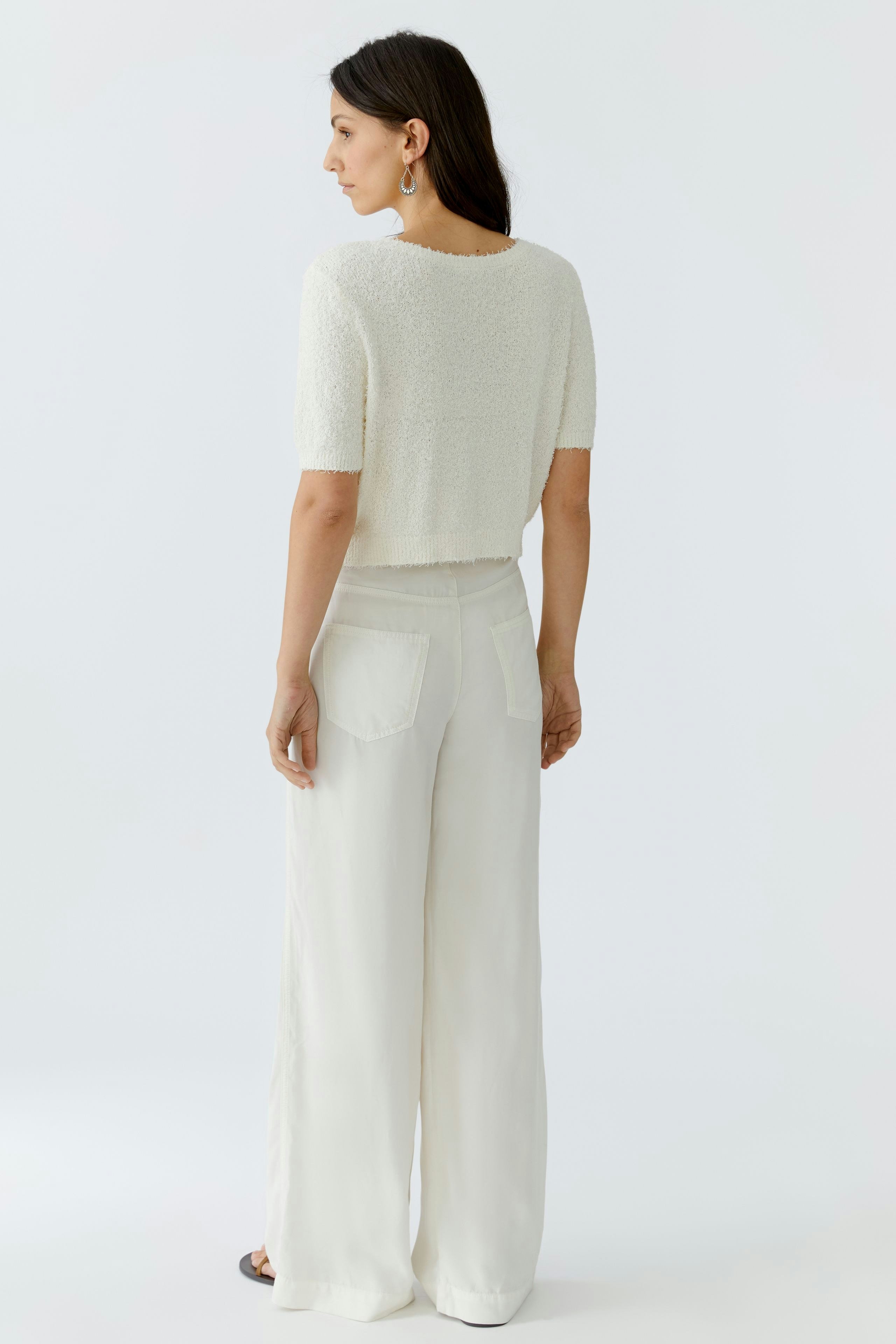 Damen-Strickjacke: Frau in kurzer, weicher Strickjacke mit lässigem Schnitt und hellen, weiten Hosen.