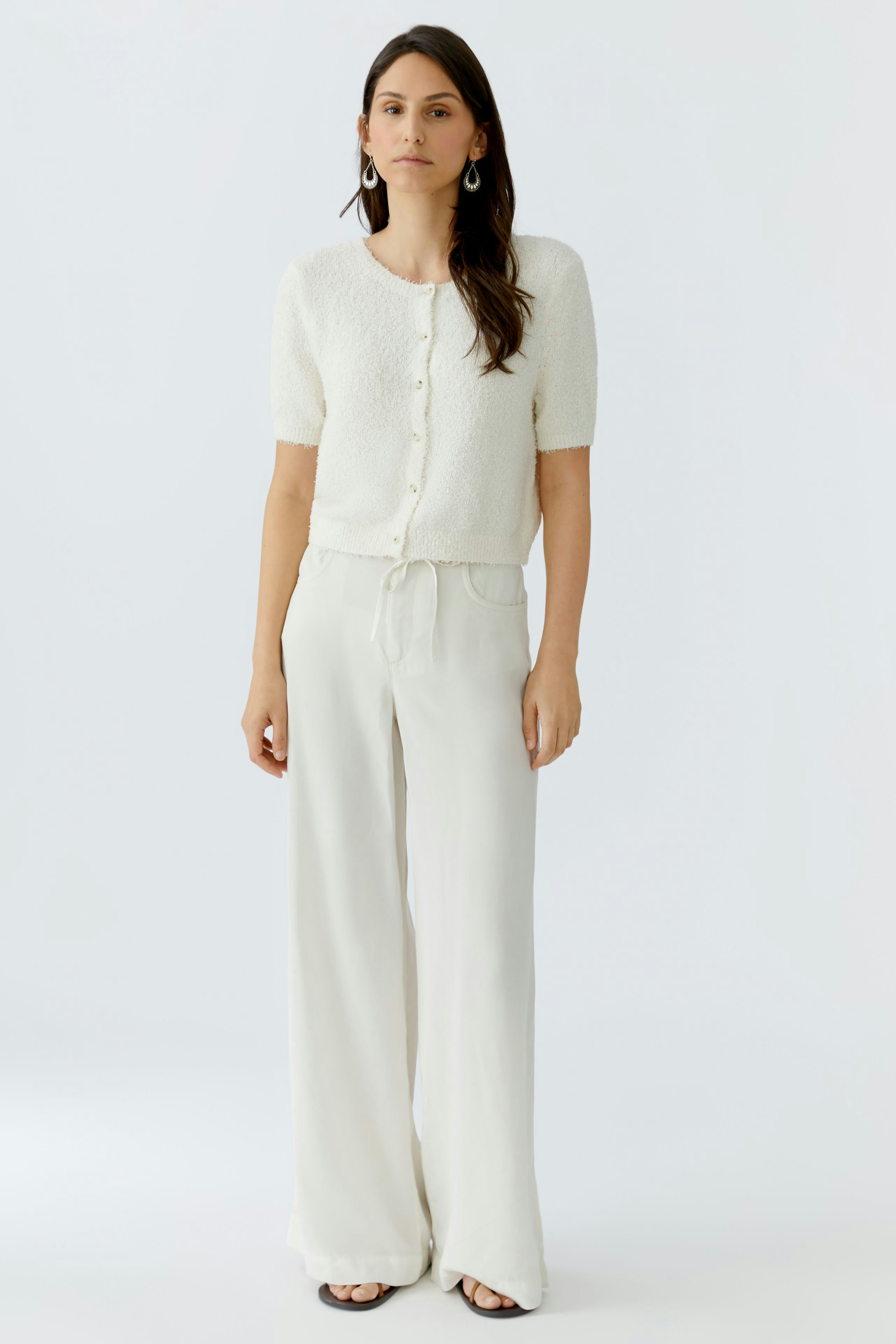 Damen-Strickjacke: Frau in weißer, kurzer Strickjacke mit Knöpfen und lässiger Hose.