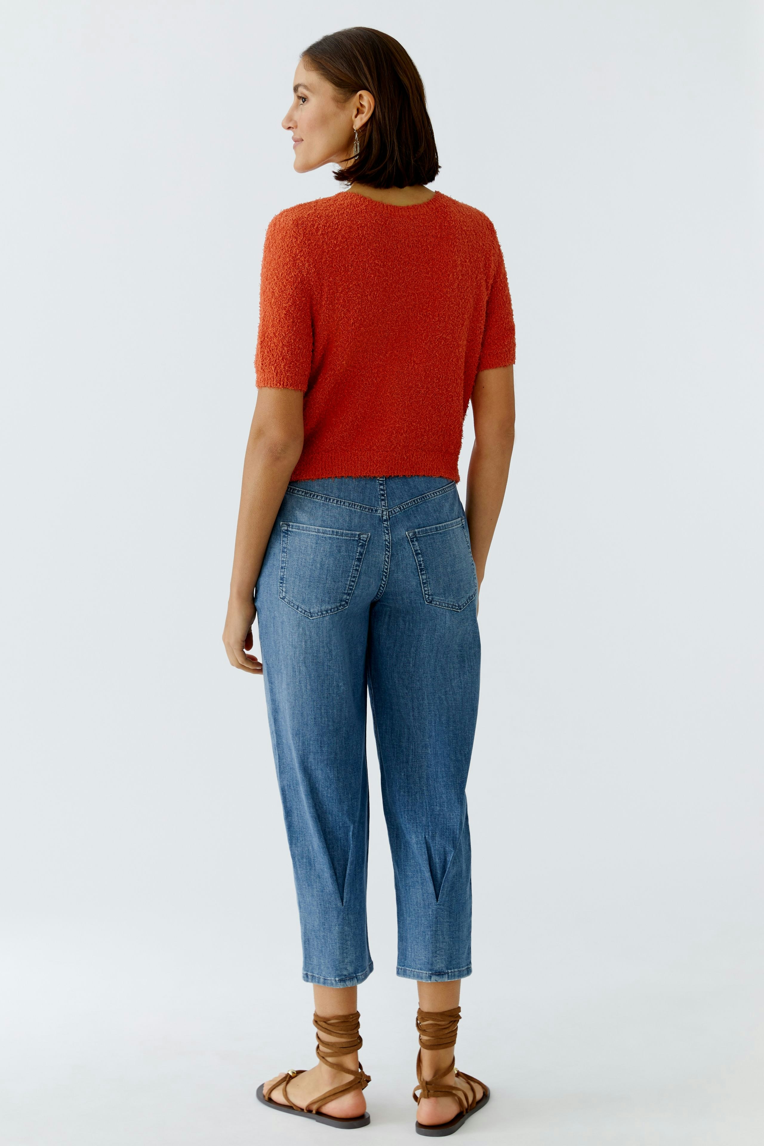 Damen-Strickjacke: Frau in roter Strickjacke mit kurzen Ärmeln und lässigen Jeans von hinten.