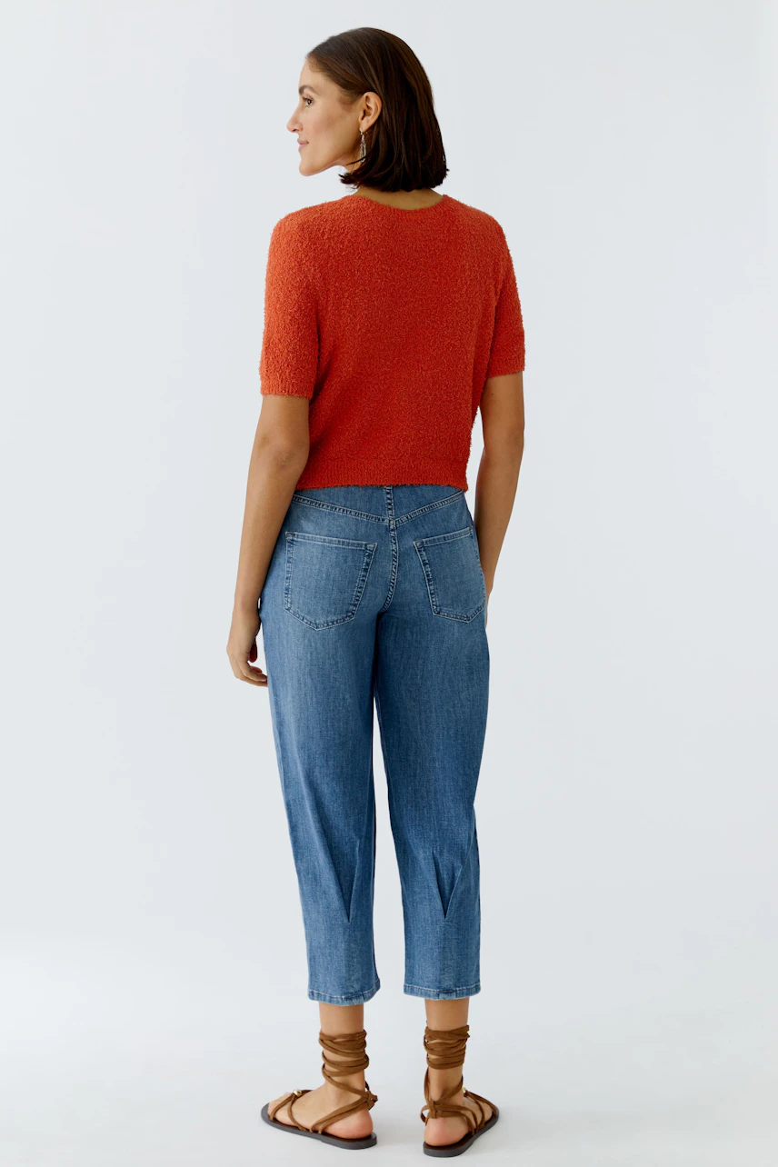 Casual women's cardigan: A woman in a short-sleeved, textured orange cardigan paired with blue jeans.