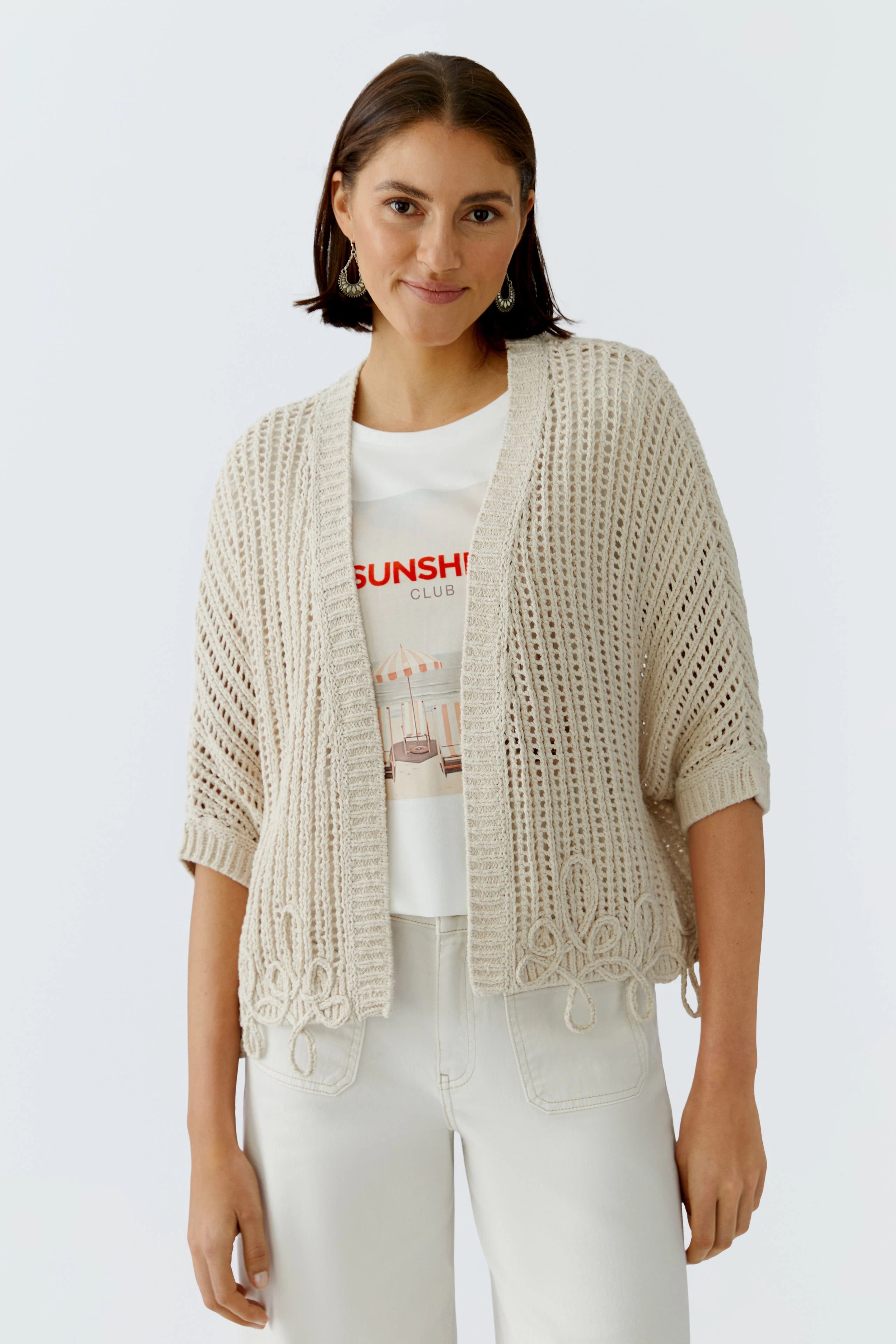 Beige Strickjacke: Frau trägt eine lockere, offene Strickjacke mit kurzen Ärmeln über einem T-Shirt.