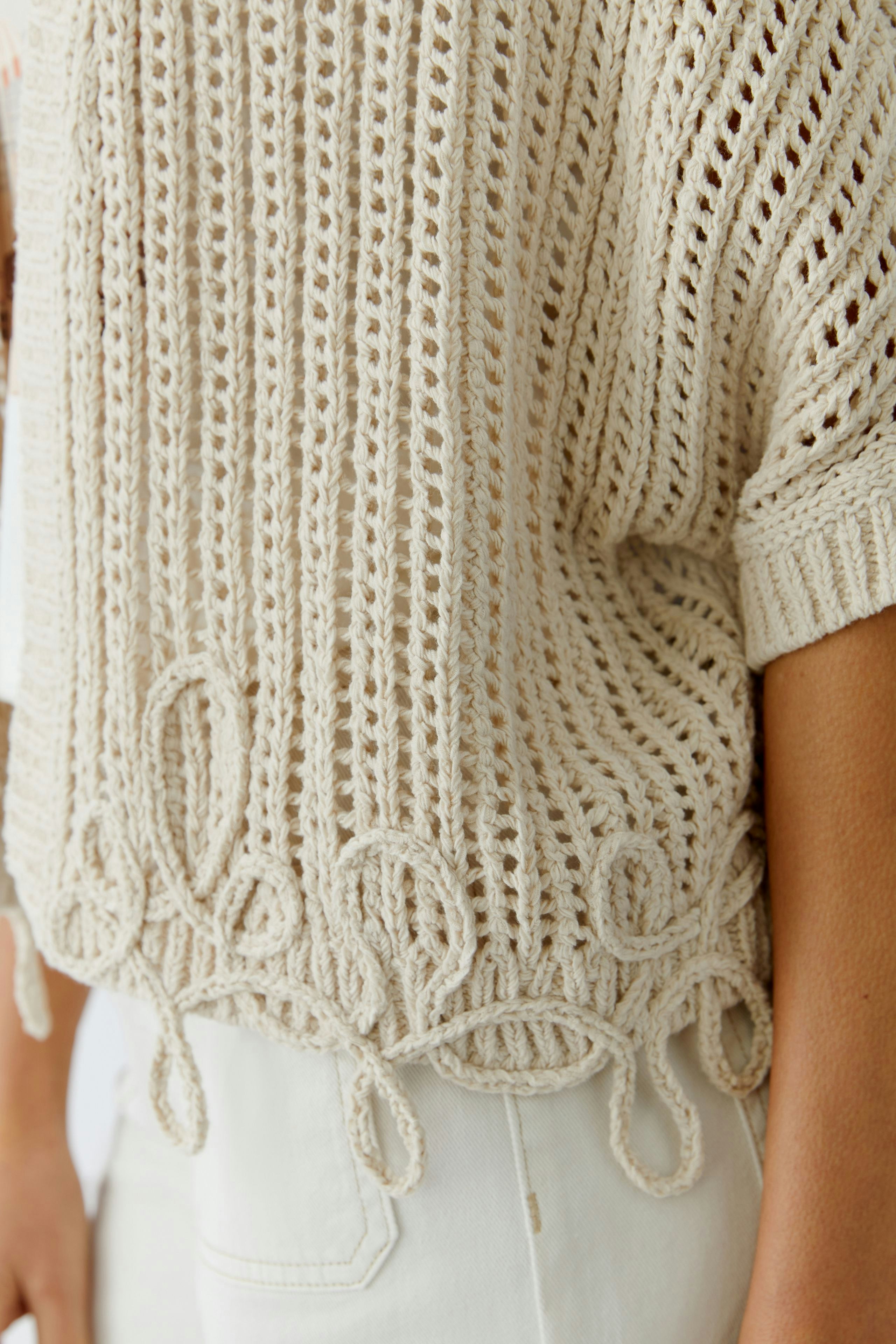 Bequeme Damen-Strickjacke in hellem Beige mit verspieltem Lochmuster und dekorativen Fransen.