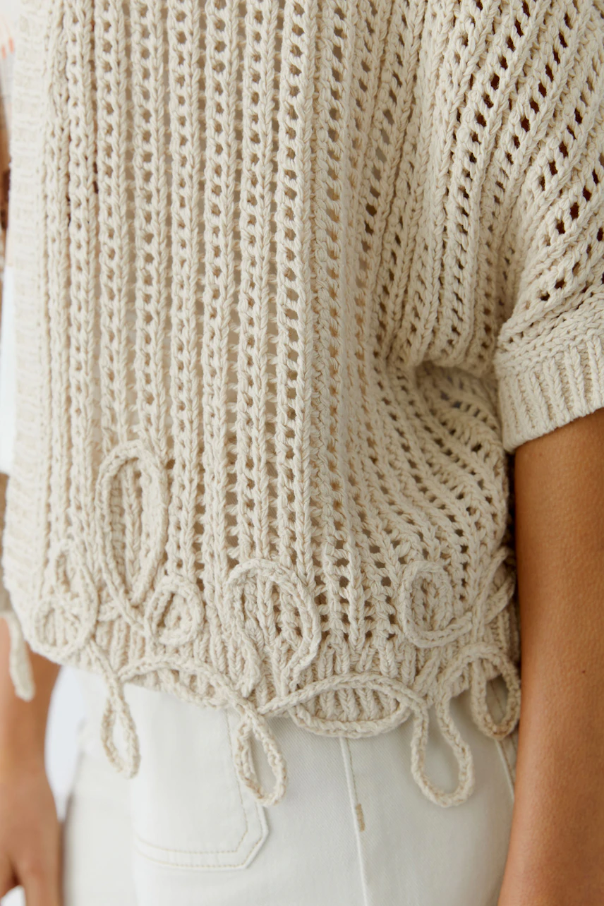 Casual women's pullover: A woman in a light beige knitted pullover with decorative loops.