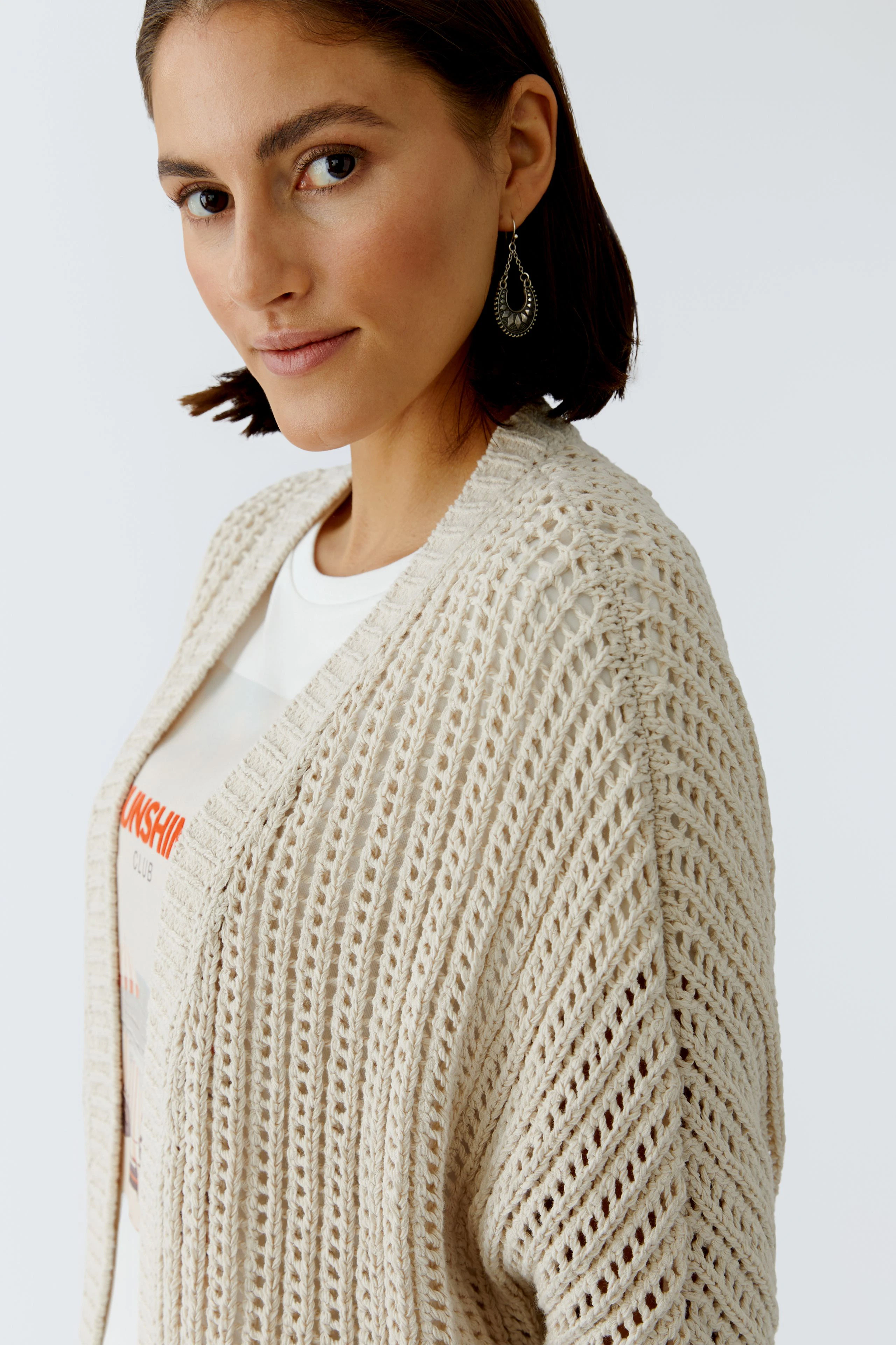 Bequeme Damen-Strickjacke: Frau mit offener, heller Strickjacke und lässigem T-Shirt blickt freundlich.