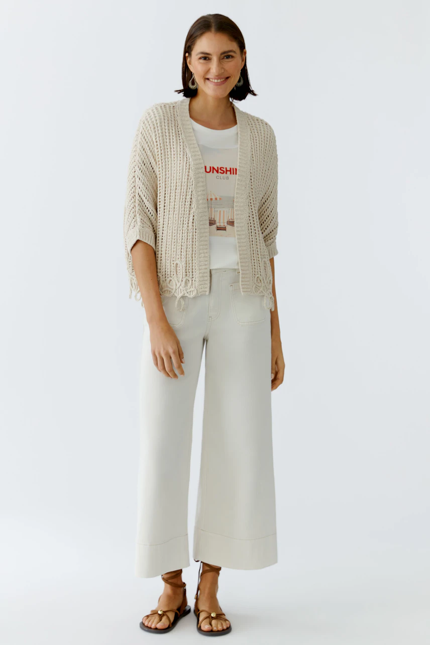 Casual women's cardigan: A woman in a light beige knitted cardigan over a graphic tee and wide pants.