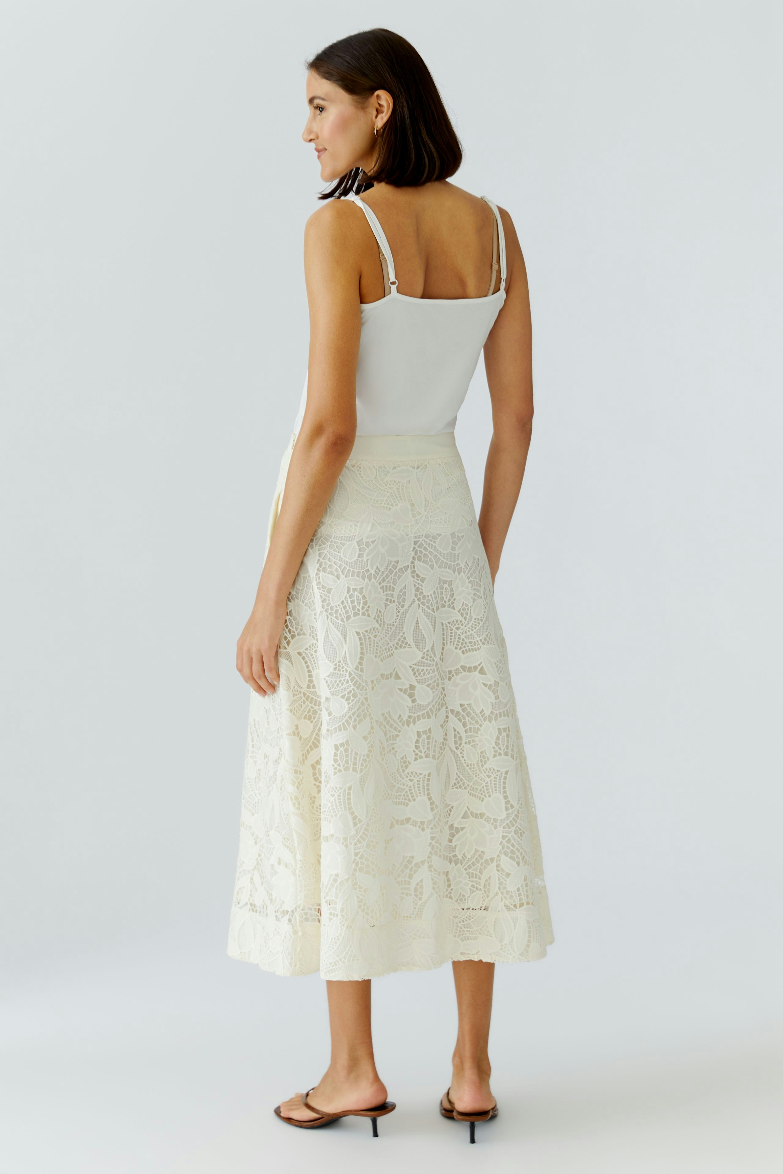 Damen A-Linien-Rock: Frau in einem hellen, floralen Rock mit Spitzen-Details und lässigem Top von hinten.