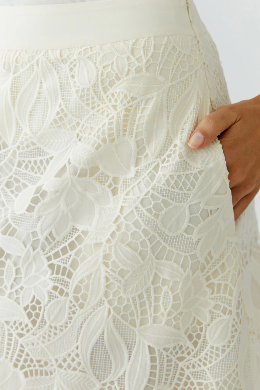 A-line skirt: Close-up of a woman’s hand on a white lace skirt with floral patterns.