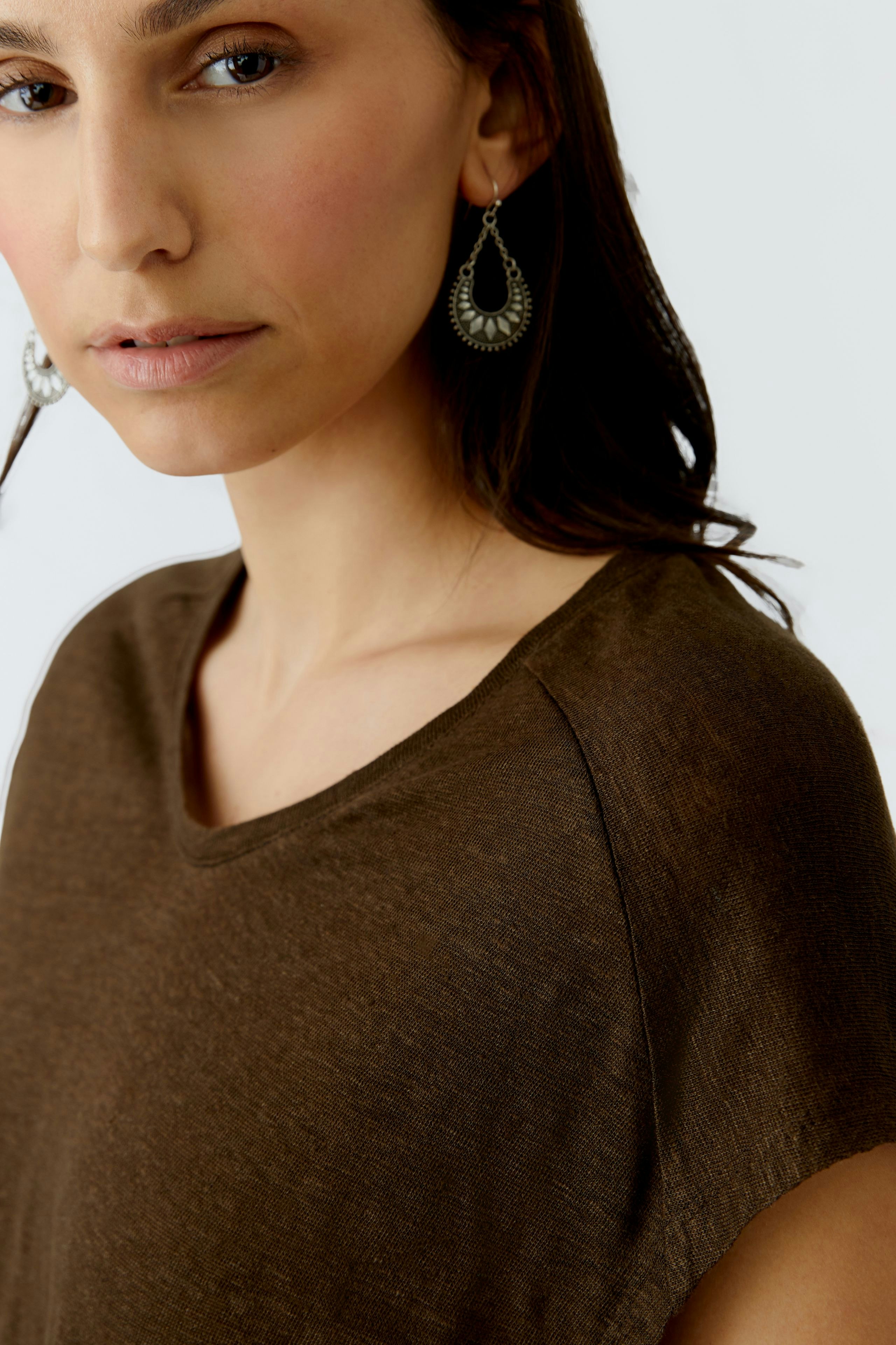 Bequeme Damen-T-Shirt: Frau mit braunem Shirt und auffälligen Ohrringen blickt direkt in die Kamera.