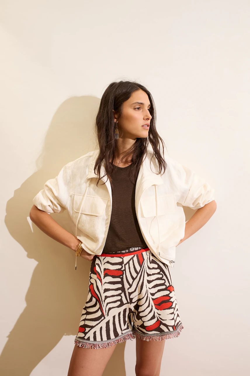 Frau im T-Shirt mit weißer Jacke und gemusterten Shorts, lässiger Look.