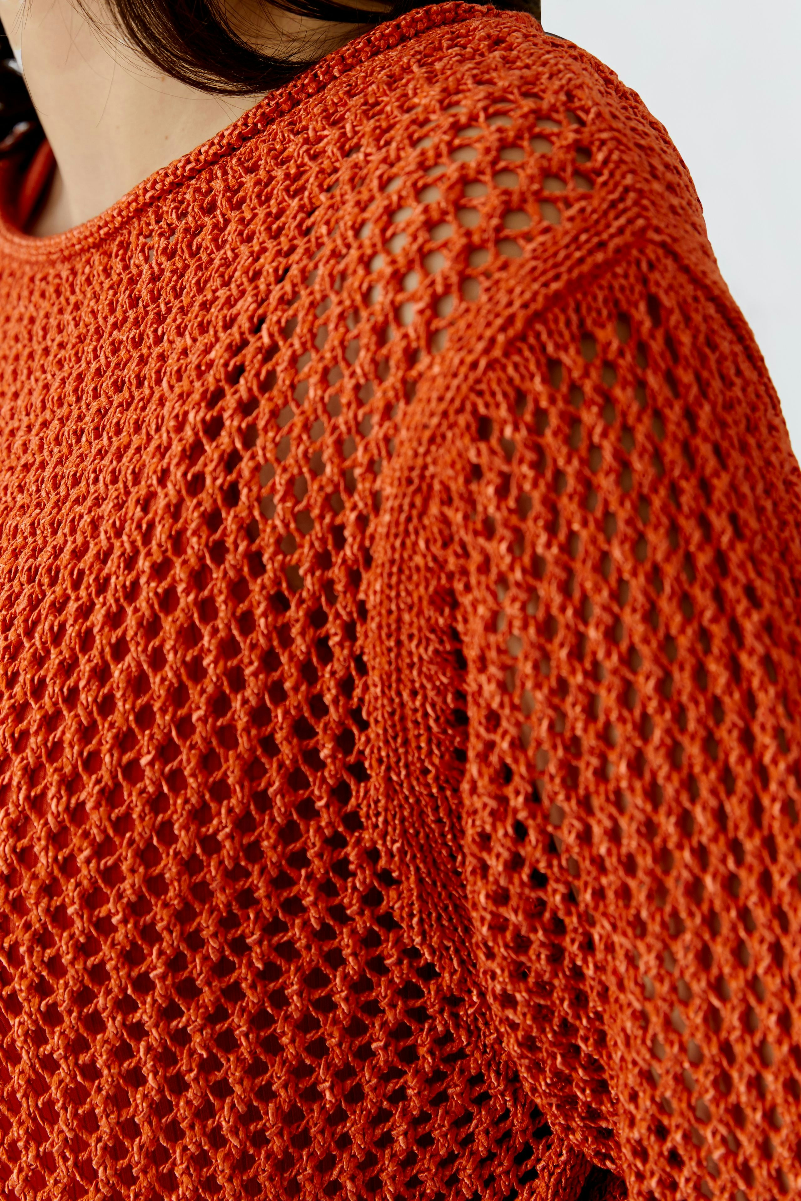 Damen-Pullover: Frau in einem lockeren, orangefarbenen Strickpullover mit Netzstruktur.
