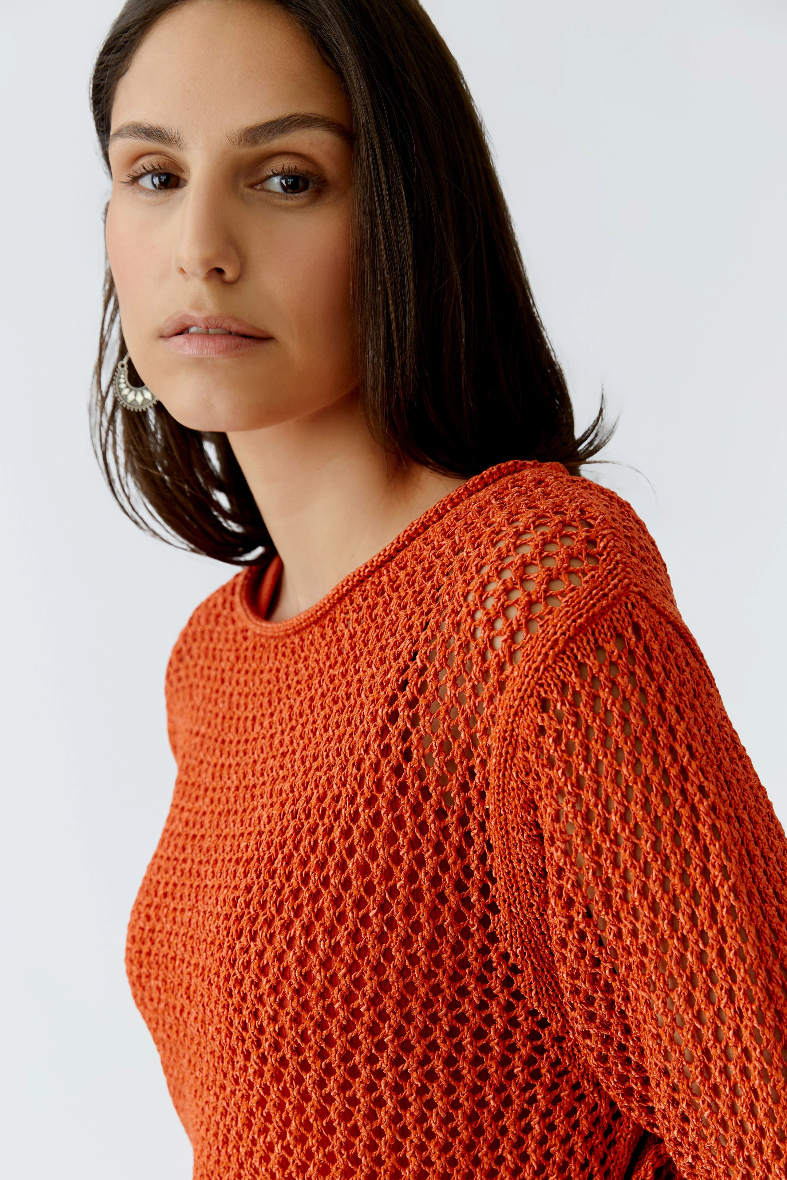 Damen-Pullover: Frau in orangefarbenem, luftigen Strickpullover mit Netzstruktur blickt direkt in die Kamera.