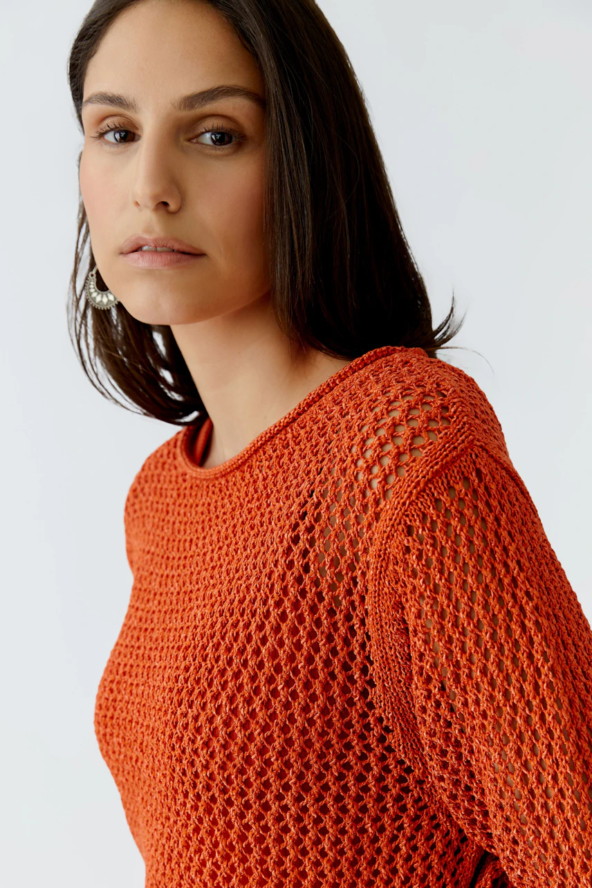 Damen-Pullover: Frau in orangefarbenem, luftigen Strickpullover mit Netzstruktur blickt direkt in die Kamera.