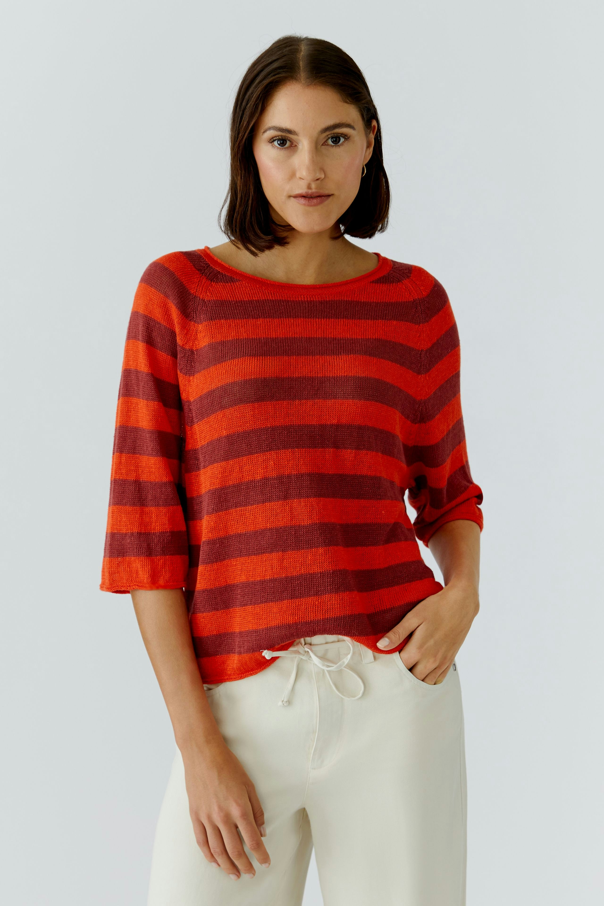 Damen-Pullover in rot mit breiten Streifen, lässig kombiniert mit hellen Hosen.