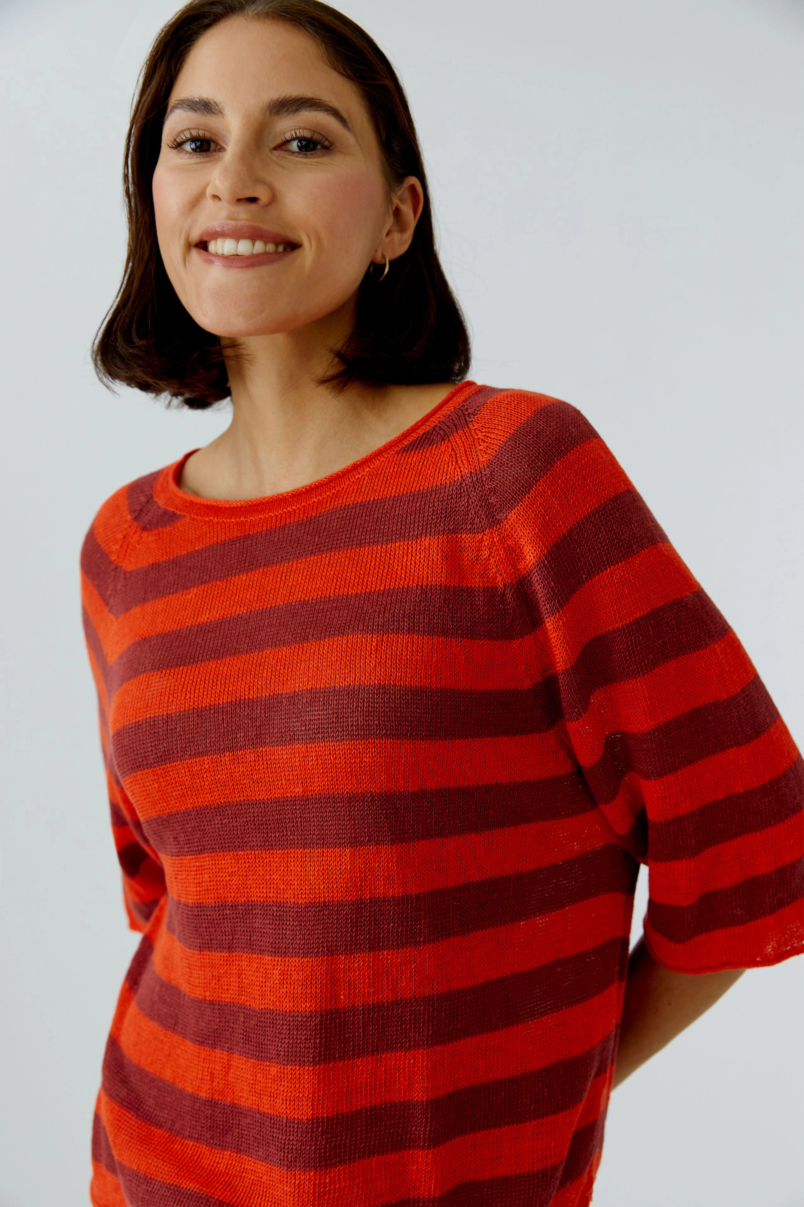 Damen-Pullover: Frau in gestreiftem Pullover in Rot- und Orangetönen lächelt freundlich.