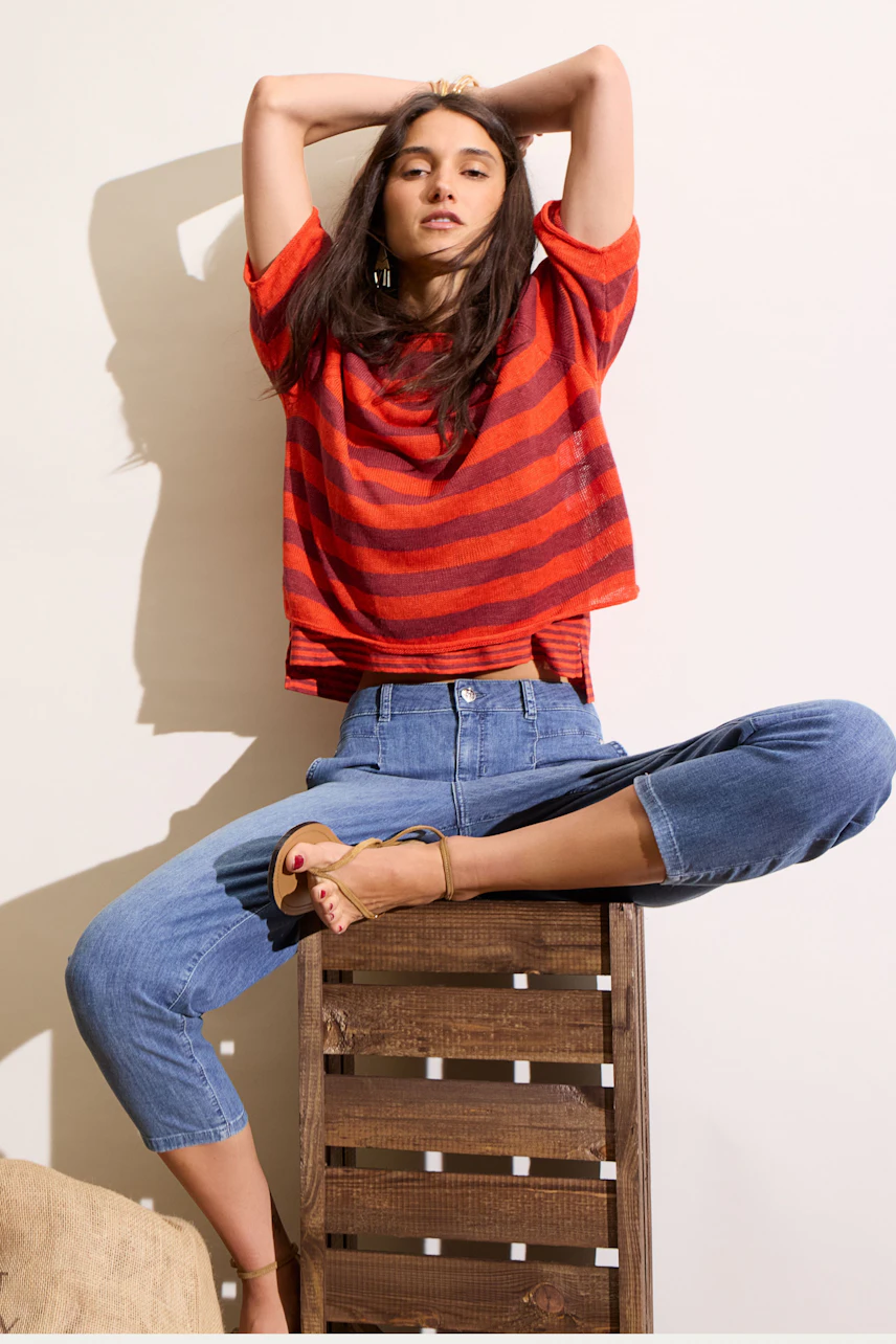 Casual women's pullover: Woman in red striped pullover, relaxed pose, paired with cropped jeans.