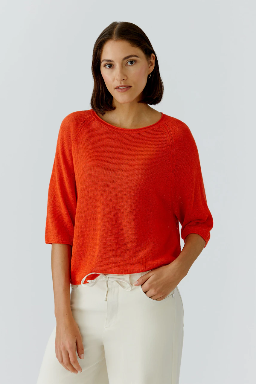 Casual women's pullover: A woman in a vibrant orange pullover with three-quarter sleeves, paired with light trousers.