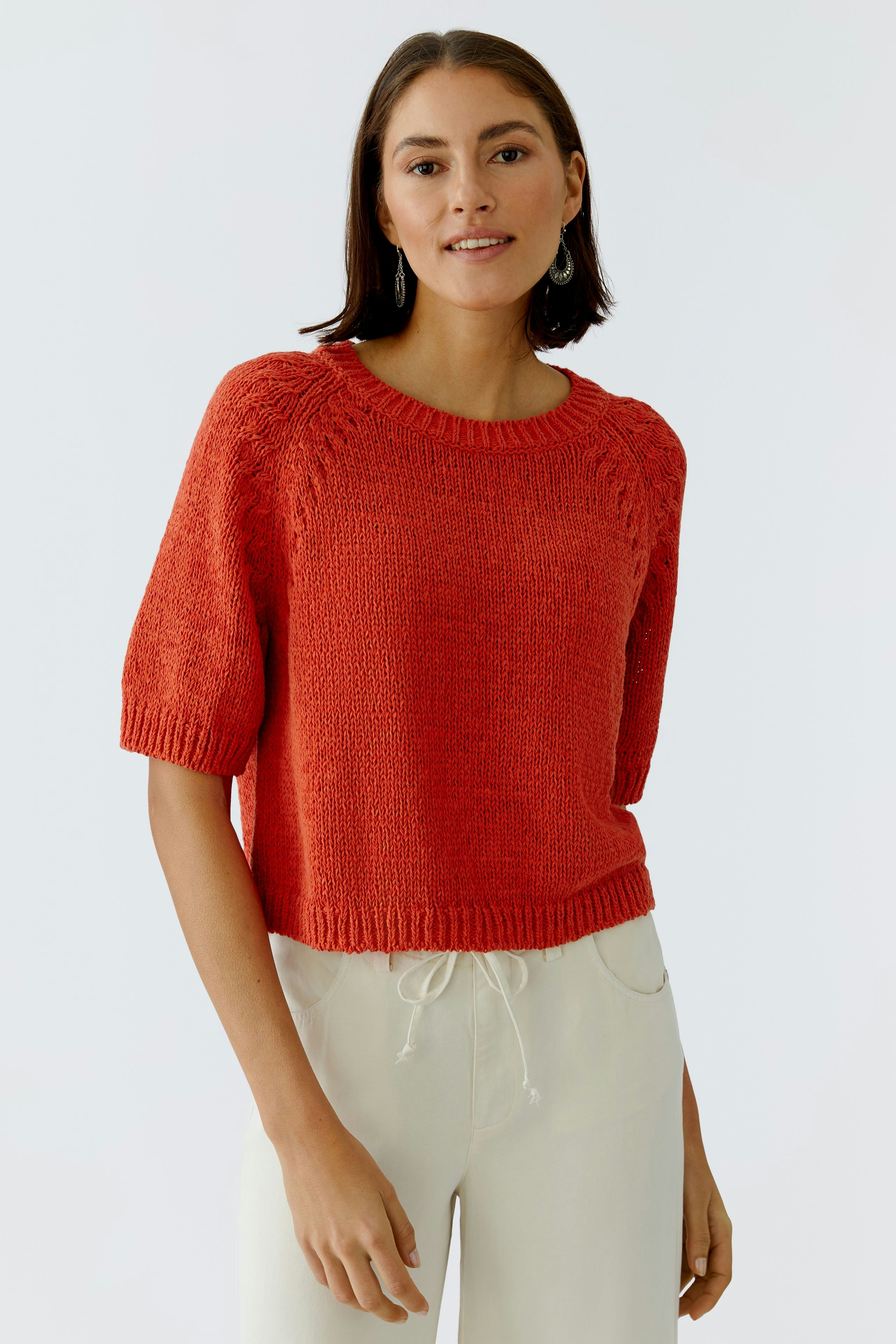 Damen-Pullover in leuchtendem Rot mit kurzen Ärmeln, lässig kombiniert mit hellen Hosen.