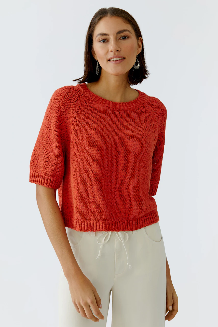 Damen-Pullover in leuchtendem Rot mit kurzen Ärmeln, lässig kombiniert mit hellen Hosen.