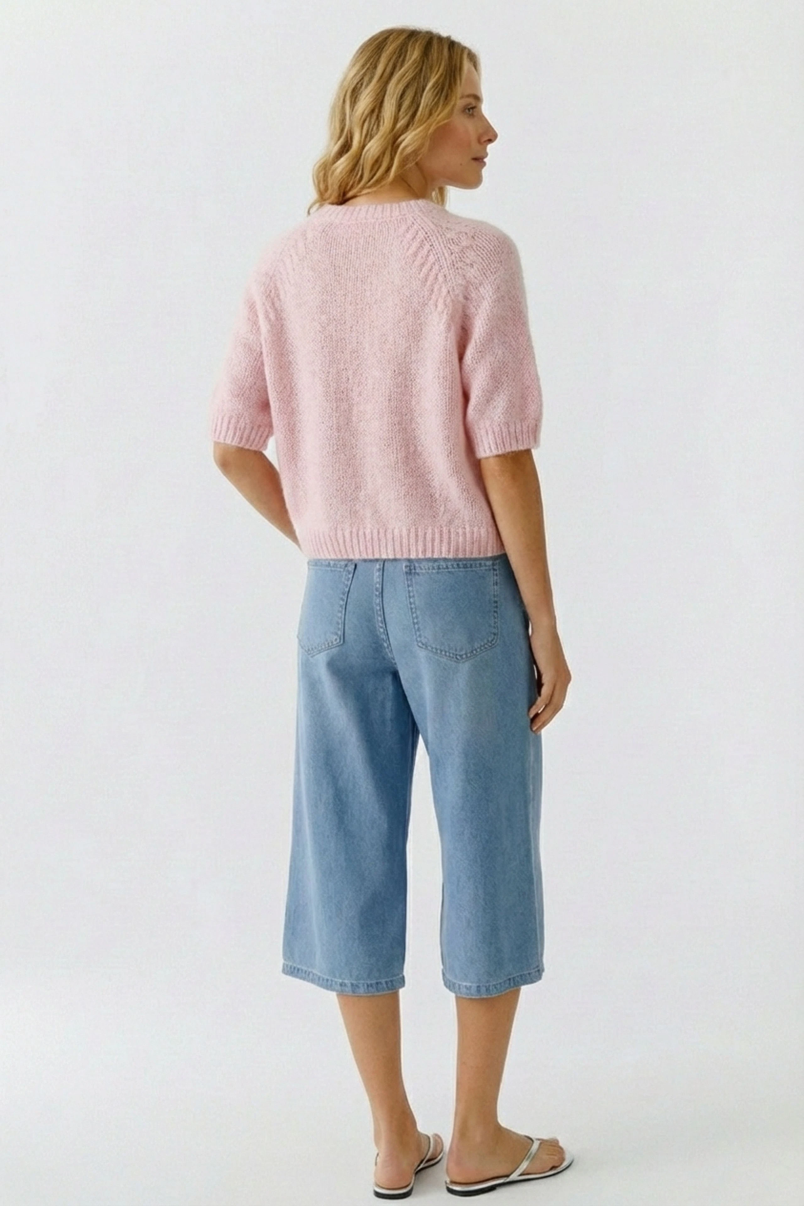 Damen-Pullover: Frau trägt einen rosa, kurzärmeligen Strickpullover mit lässigem Schnitt.