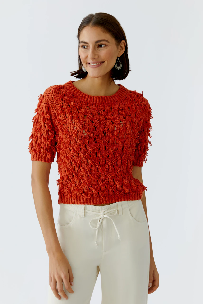 Casual women's pullover: Smiling woman in a textured red pullover paired with light trousers.