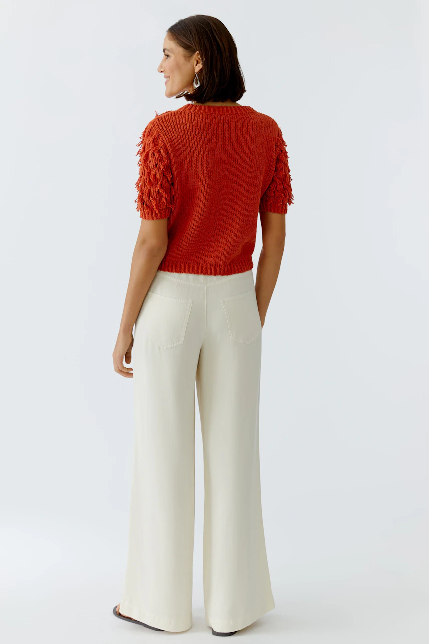 Casual women's pullover: A woman in a short-sleeved, textured orange pullover with wide white pants.
